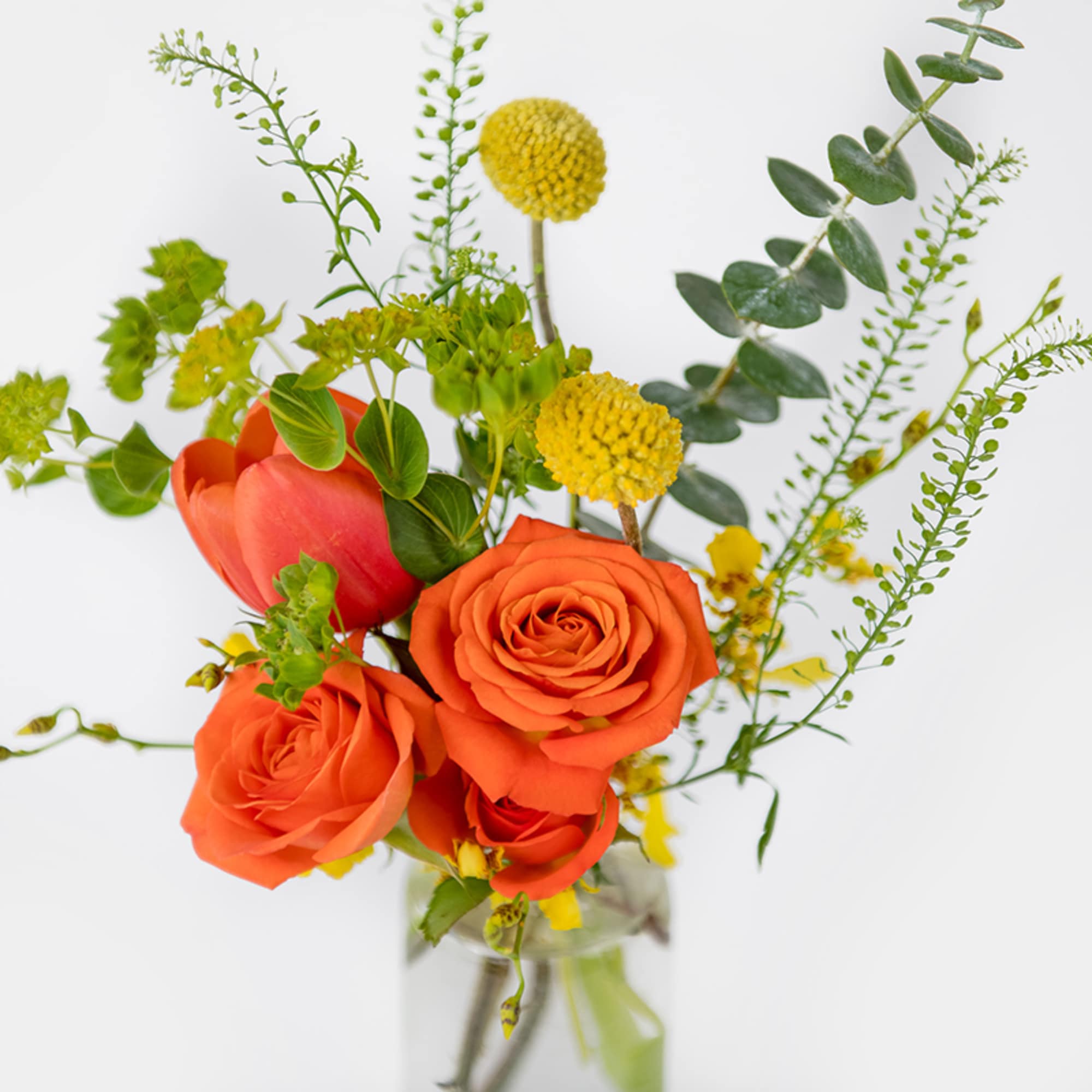 Bright arrangement of orange roses and tulips with yellow accents in a clear glass vase