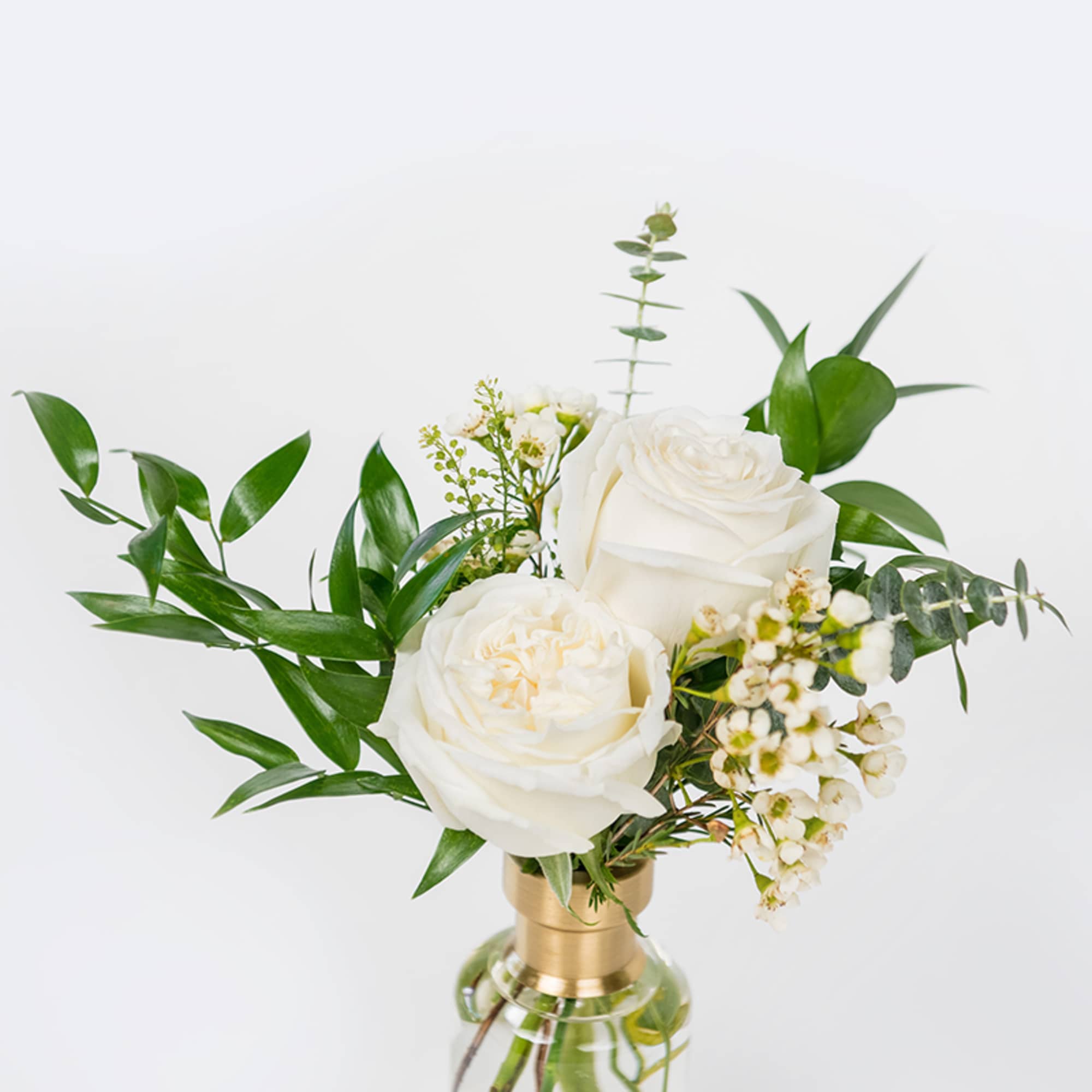 White roses arranged in a clear glass vase with greenery