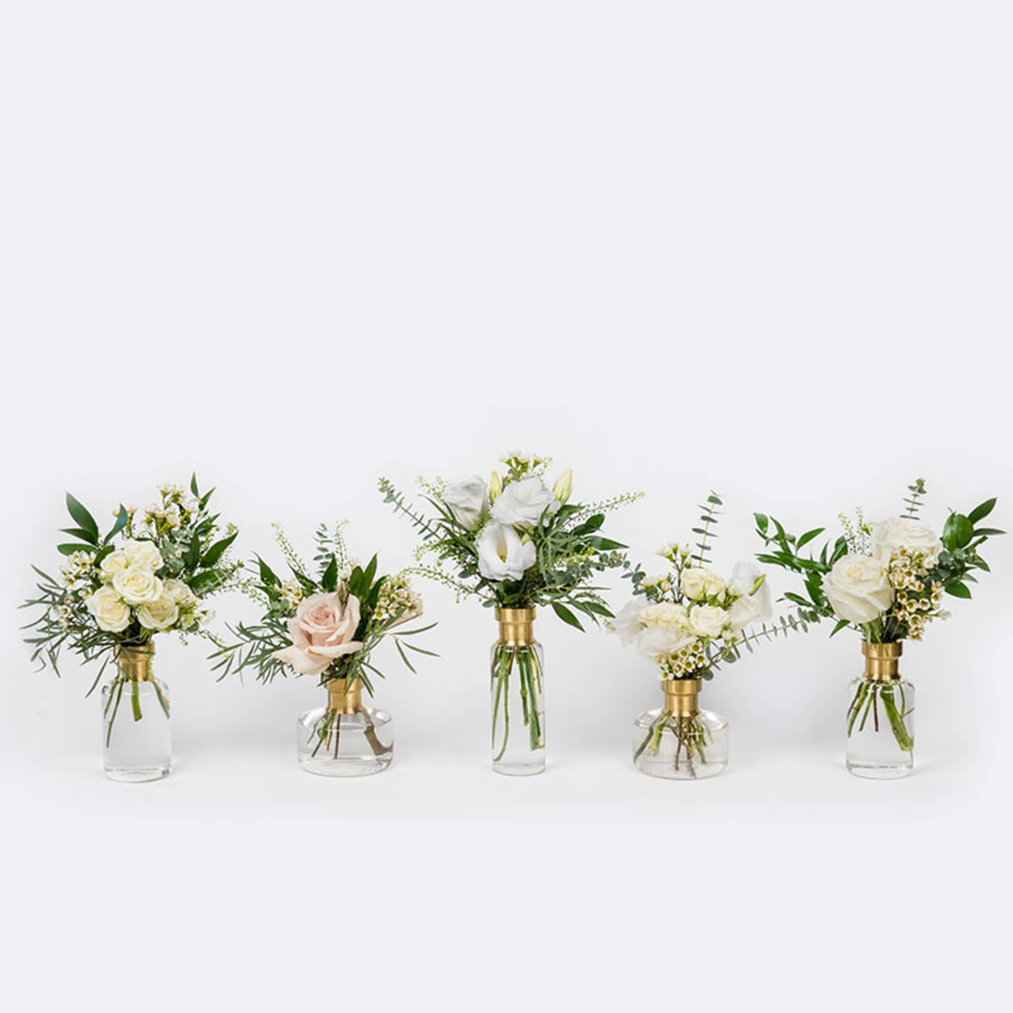Five small floral arrangements in clear glass vases with white and blush blooms