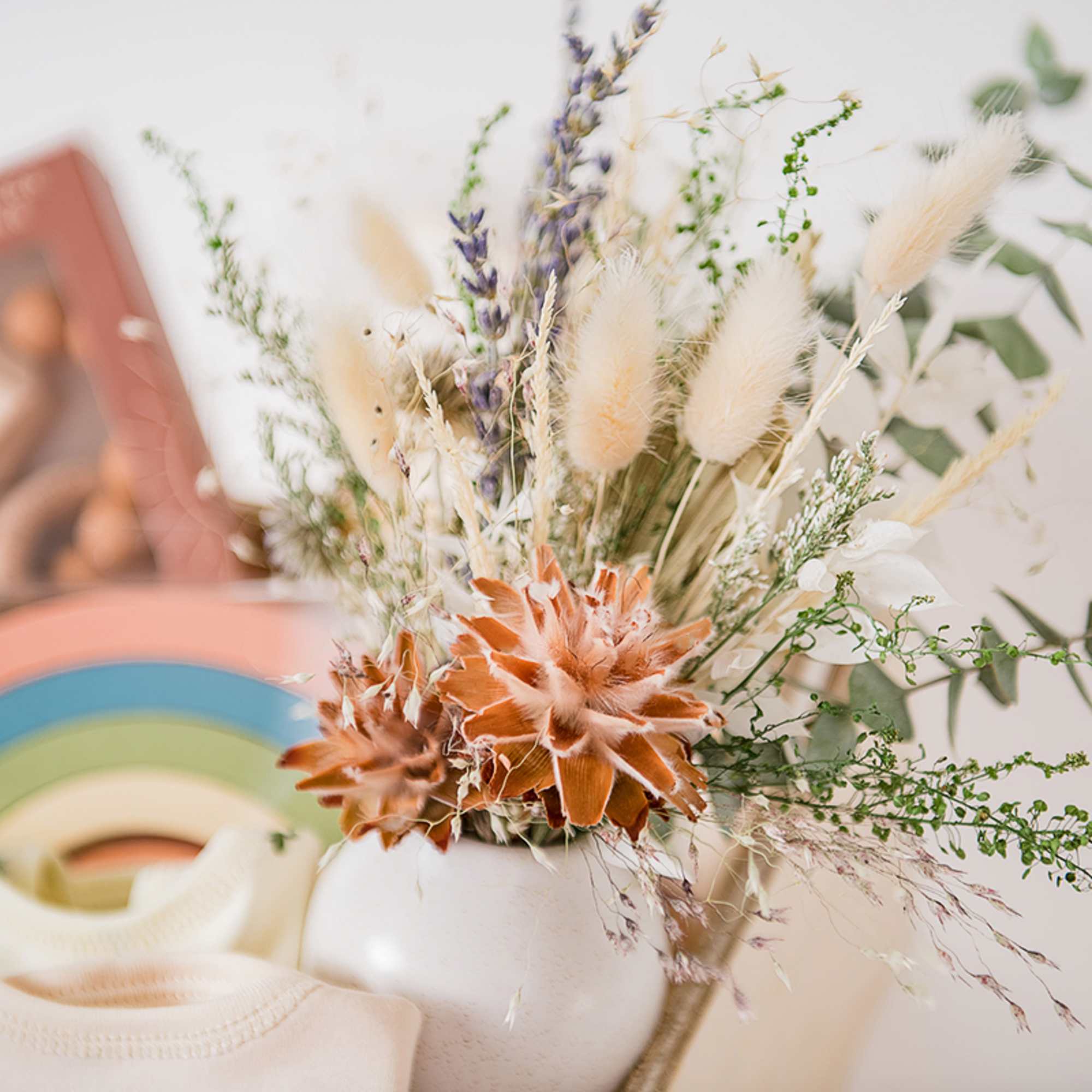 Dried floral arrangement in a white vase with orange blooms and beige grasses