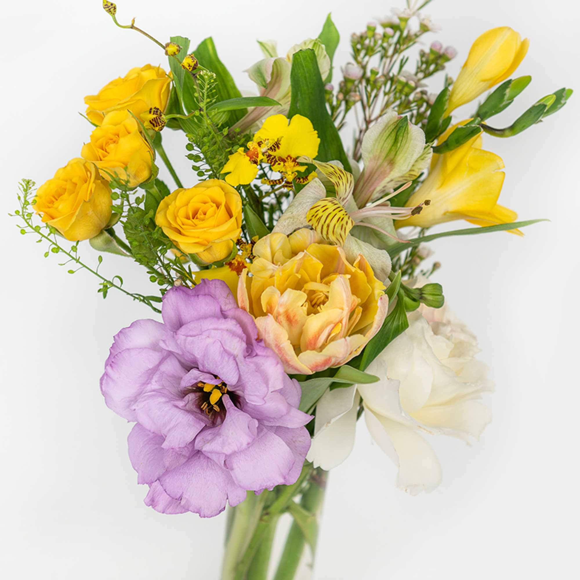 Mixed bouquet of yellow roses, lavender lisianthus, orchids and other blooms in a clear glass vase