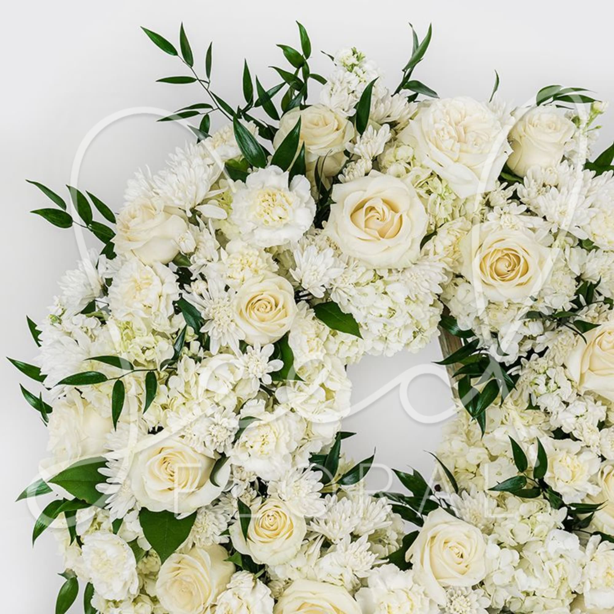 White roses and chrysanthemums arranged in a wreath with green leaves