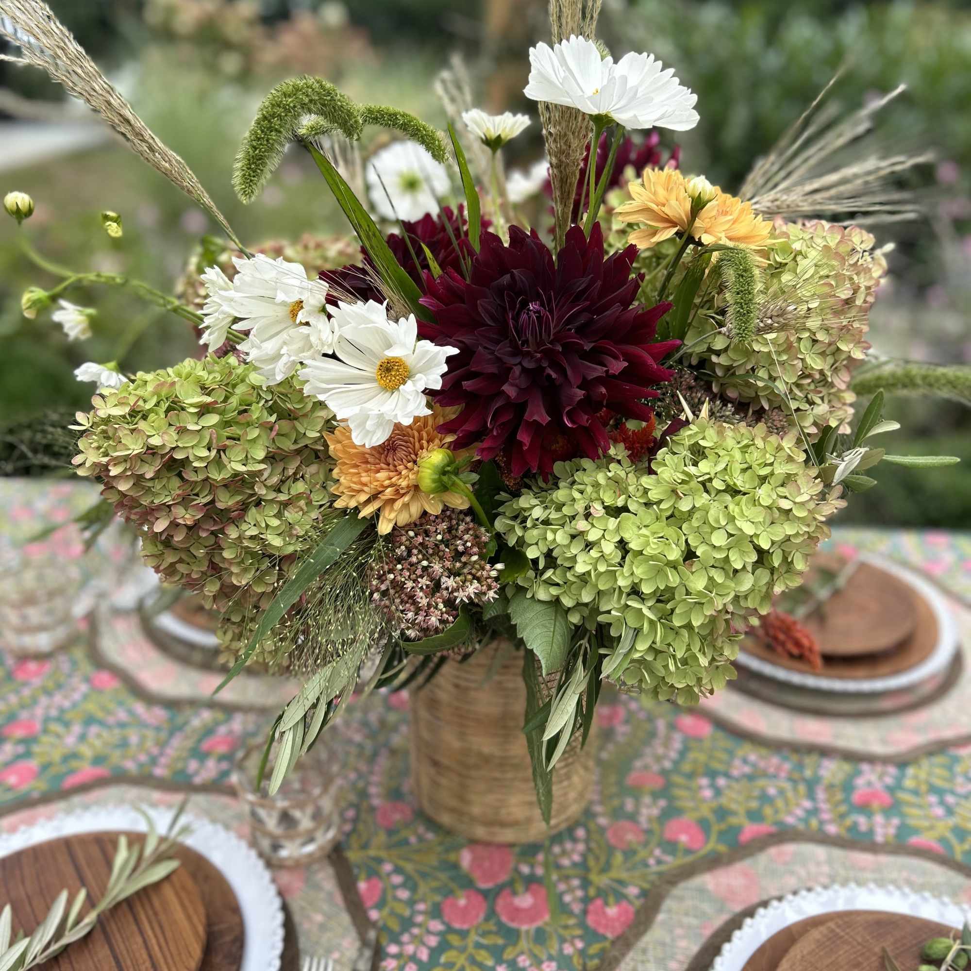 Mixed floral centerpiece with burgundy, white, and green blooms in a woven vase