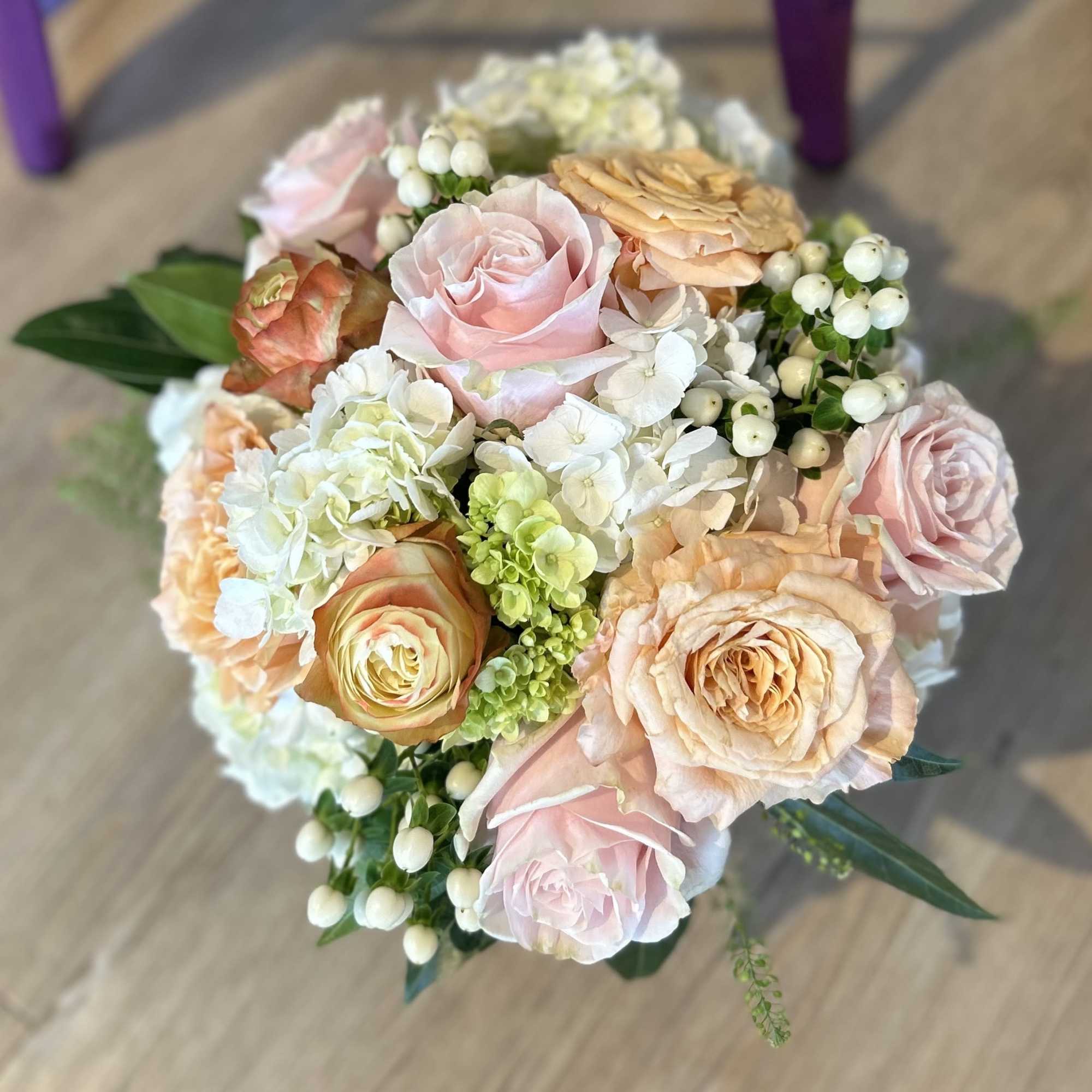 Bouquet of blush and peach roses with white hydrangeas and berry accents