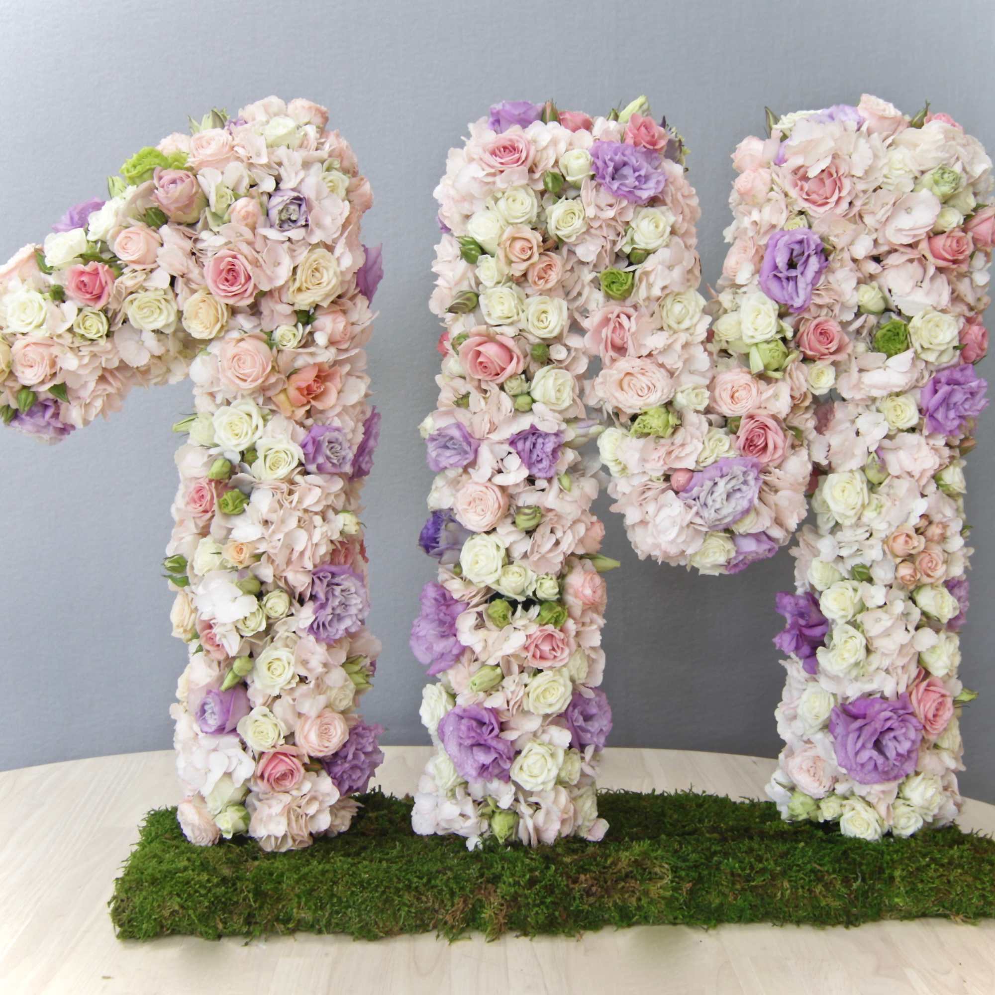 Large standing '1M' floral sculpture in pastel roses and blooms on a moss-covered base