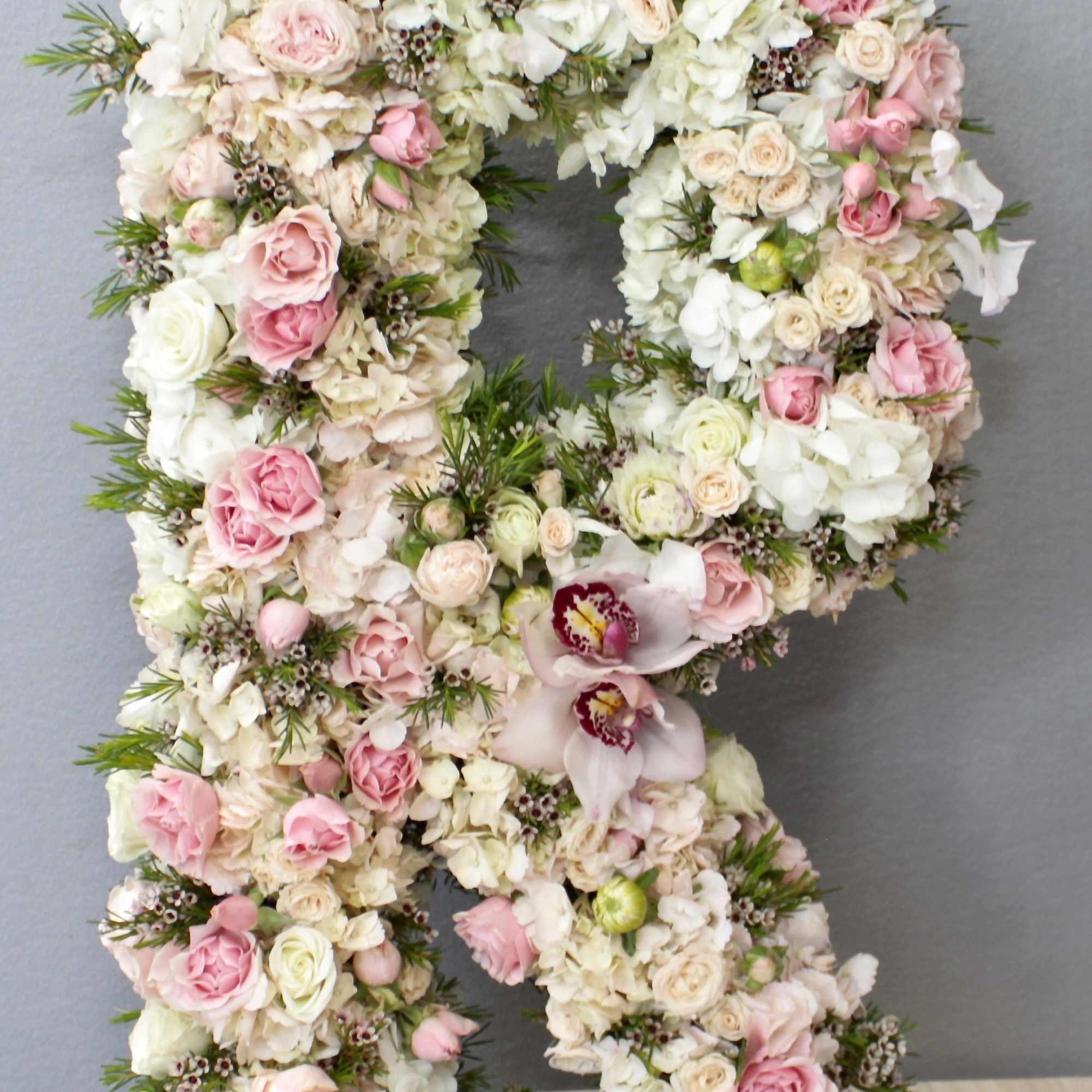Standing floral letter R made of white and blush pink roses, hydrangeas, and orchids on a mossy base.