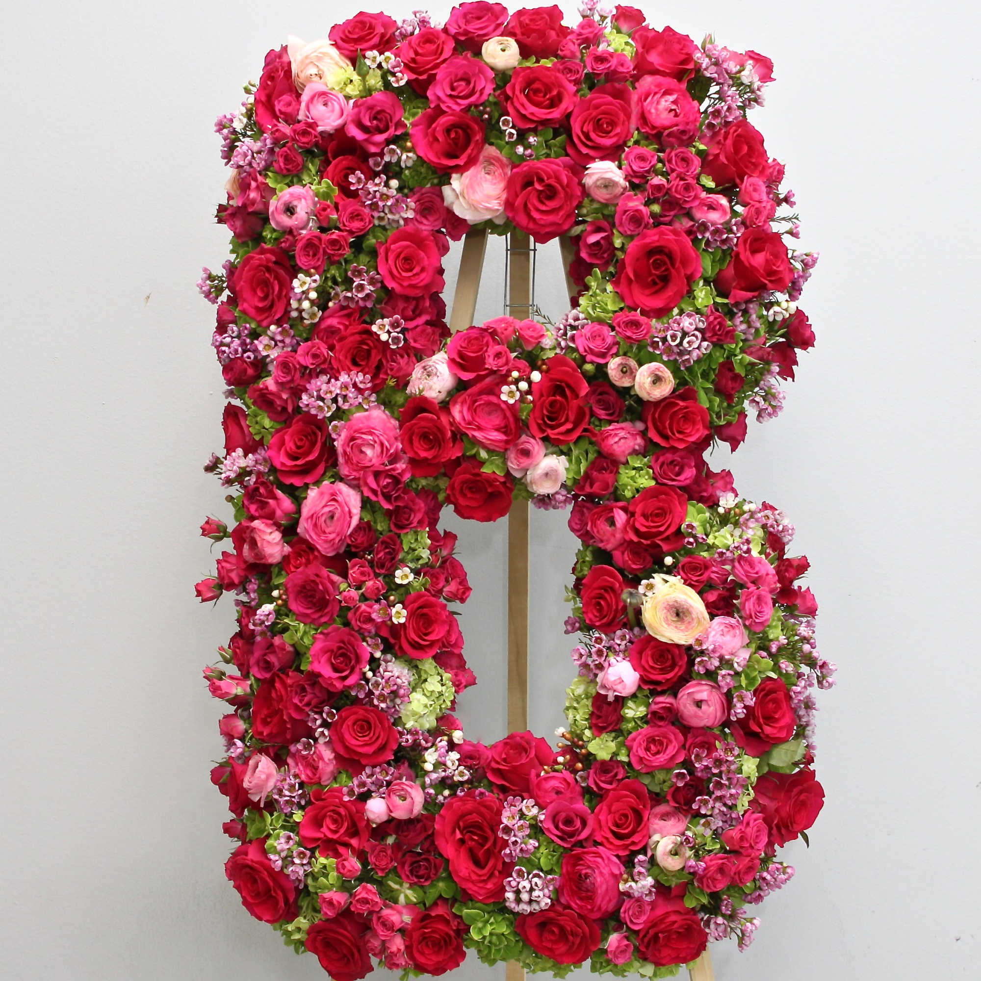 Standing floral letter B made of dense red and pink blooms on a wooden easel