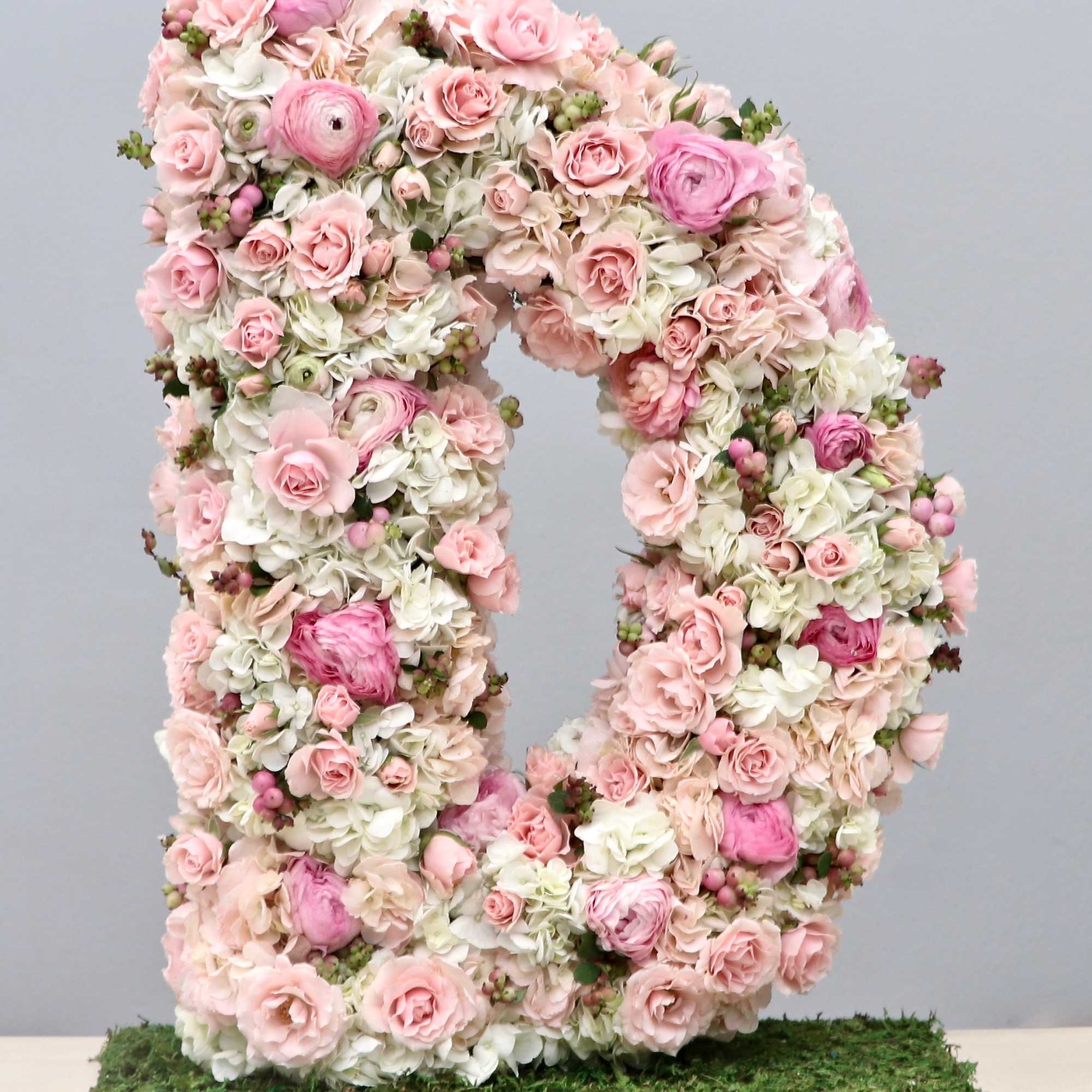 Large floral letter D made of pink and white flowers on a moss-covered base