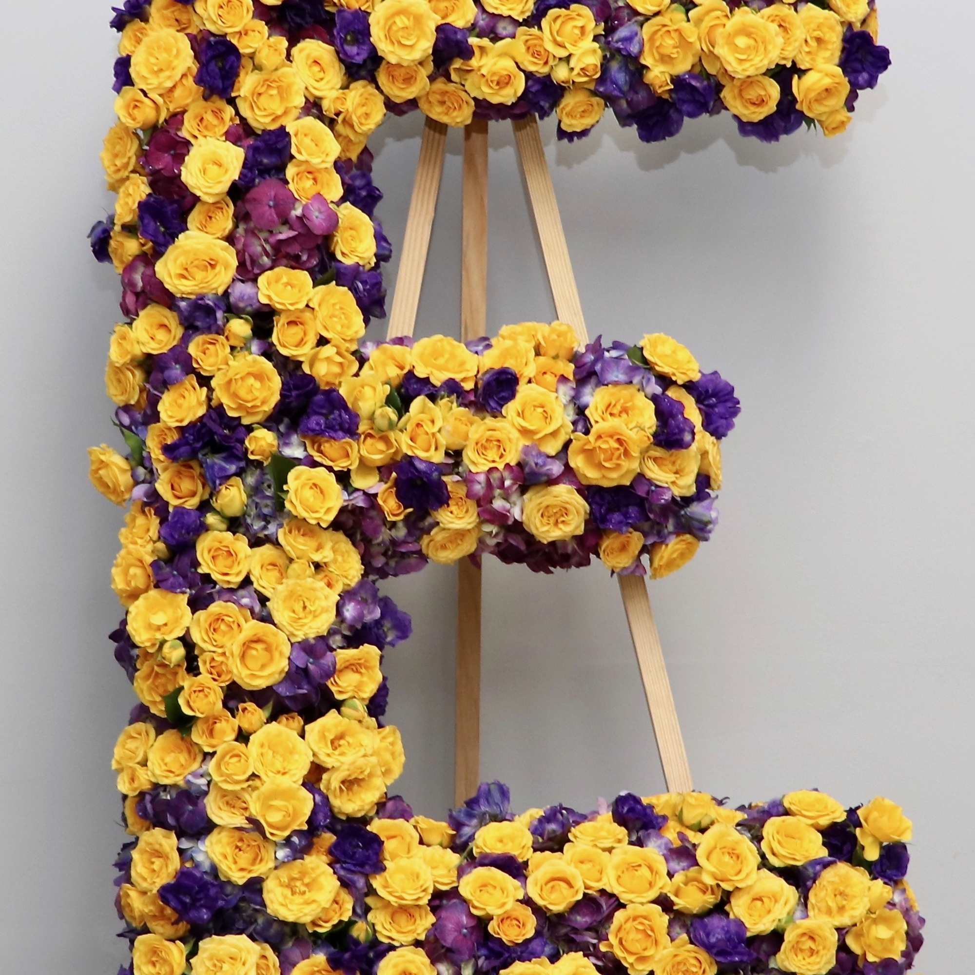 Large standing floral letter E made of yellow and purple blooms on a wooden easel
