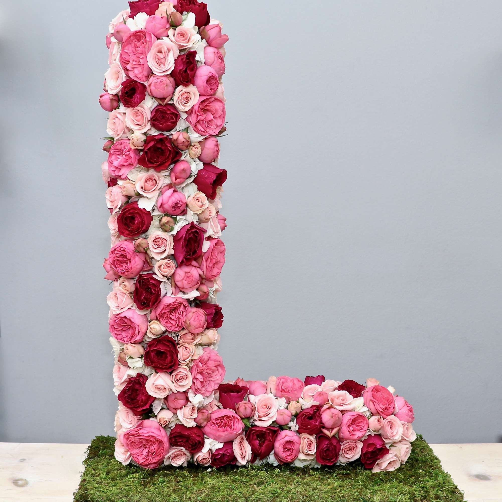 Tall letter L made of pink and red roses on a moss-covered rectangular base