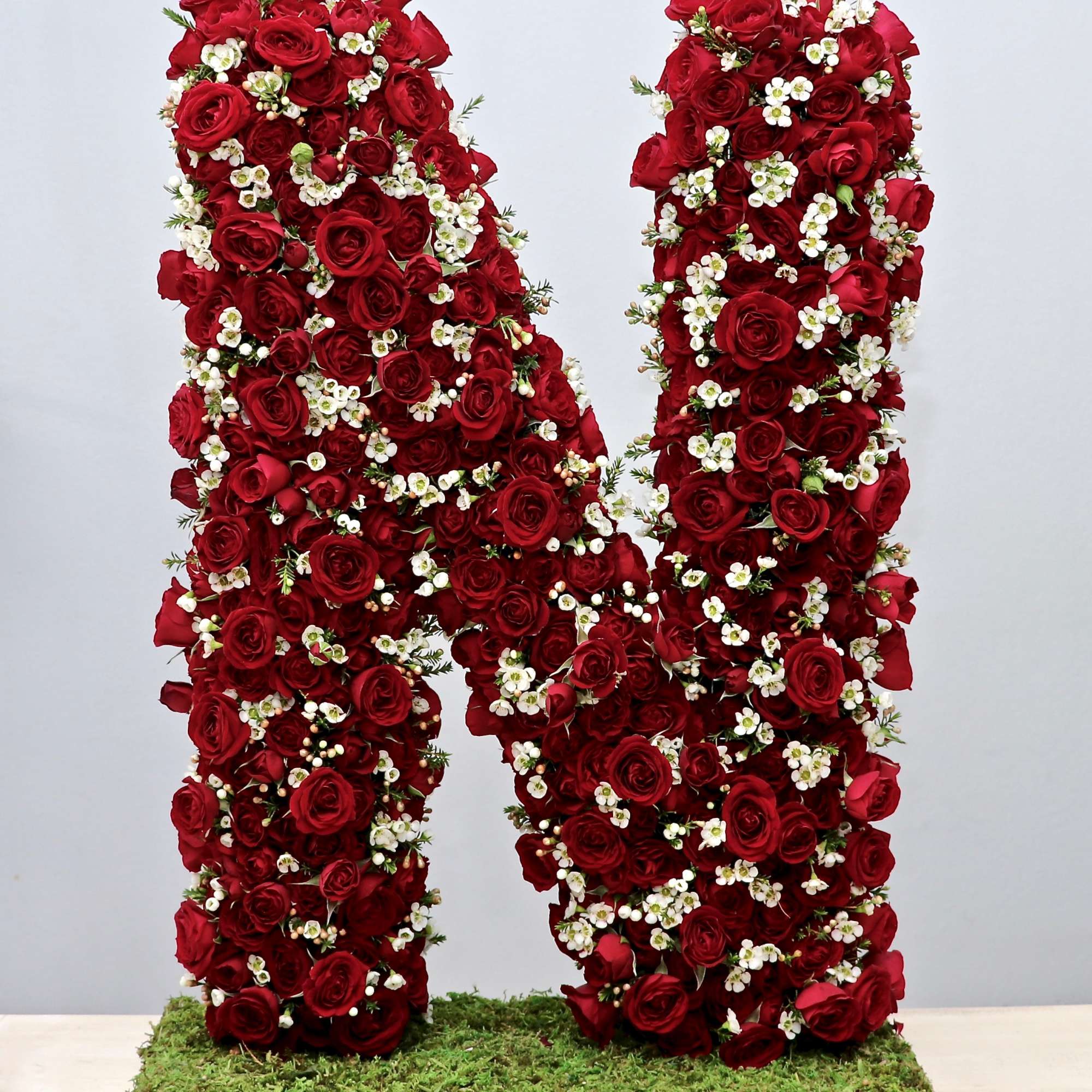 Standing floral letter N made of red roses and small white blossoms on a moss-covered base