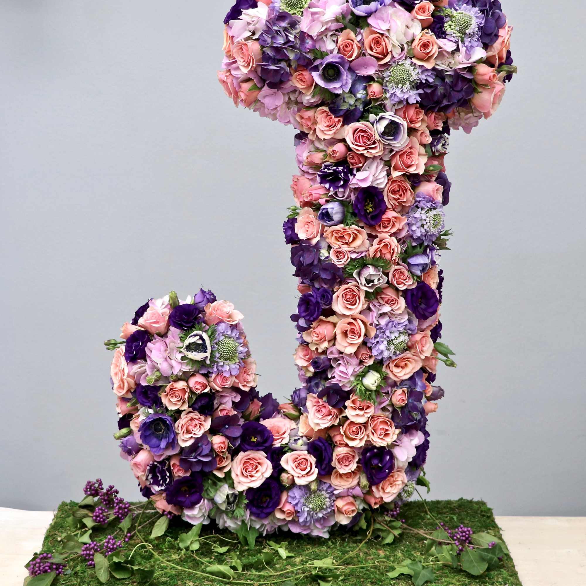 Tall floral letter J in pink and purple flowers on a moss-covered base