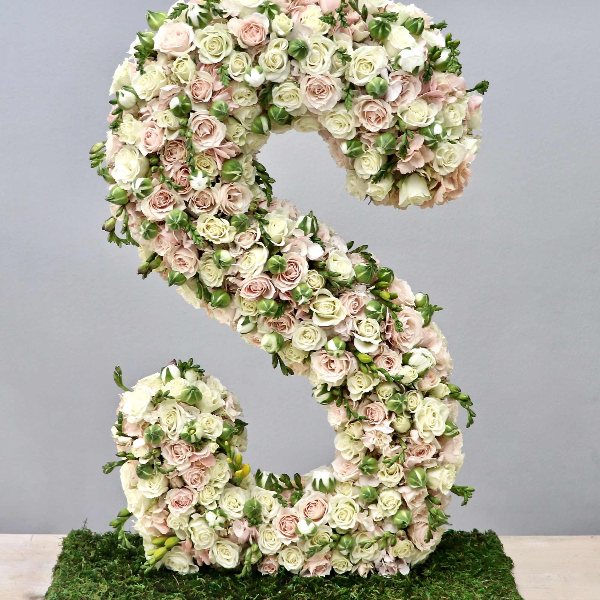 Tall floral letter S made of cream and blush roses on a moss-covered rectangular base