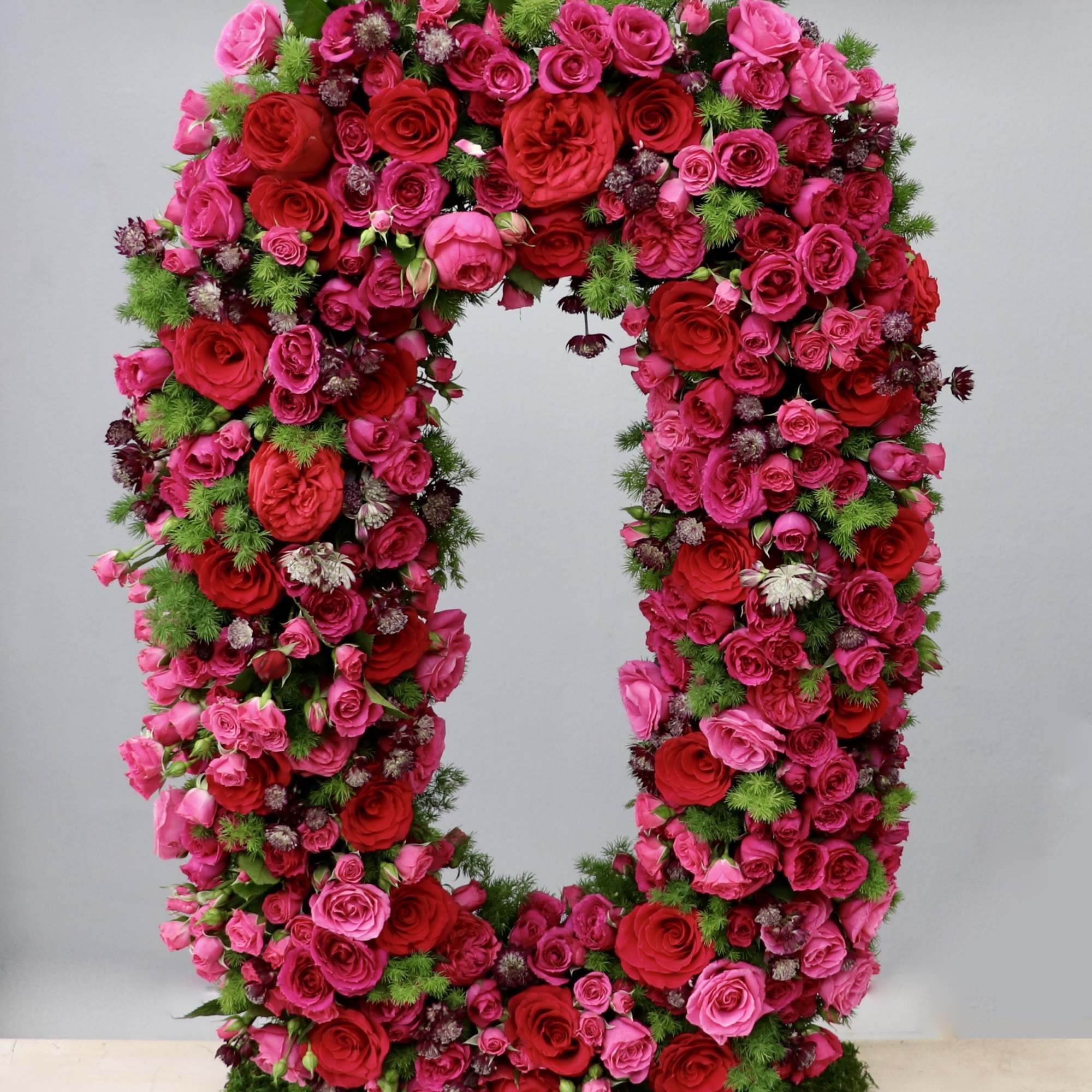 Tall oval wreath of red and hot pink roses on a moss-covered base
