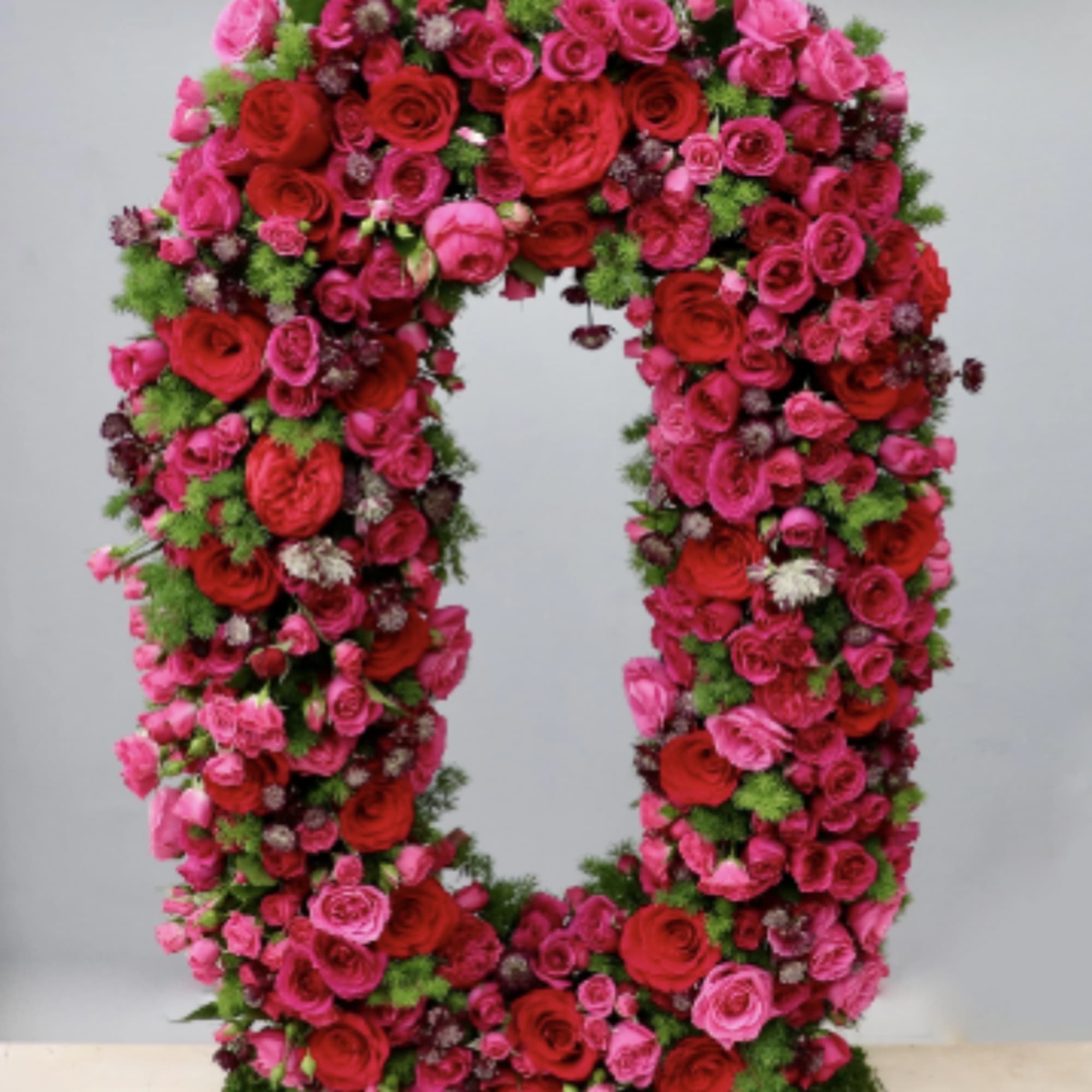 Large standing oval wreath of red and pink roses on a green moss-covered base
