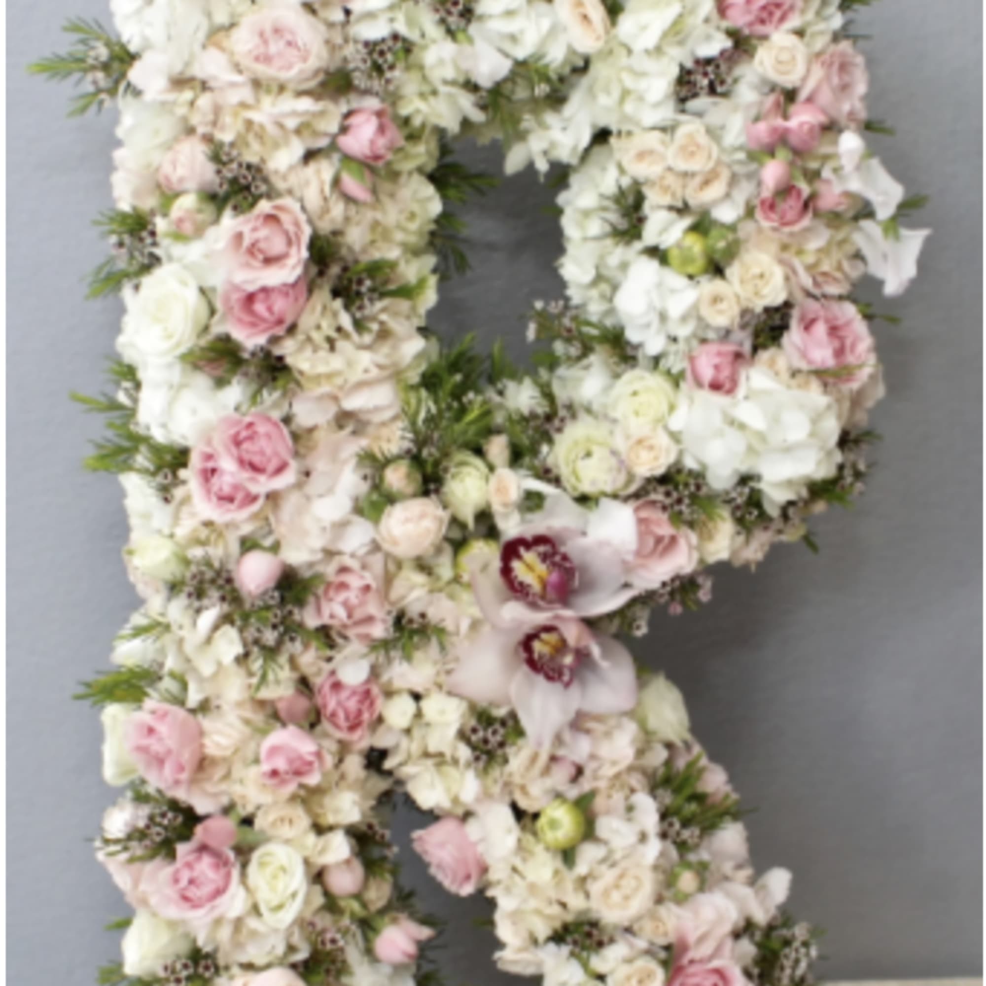 Standing floral letter R made of pink and white blooms on a moss-covered base.