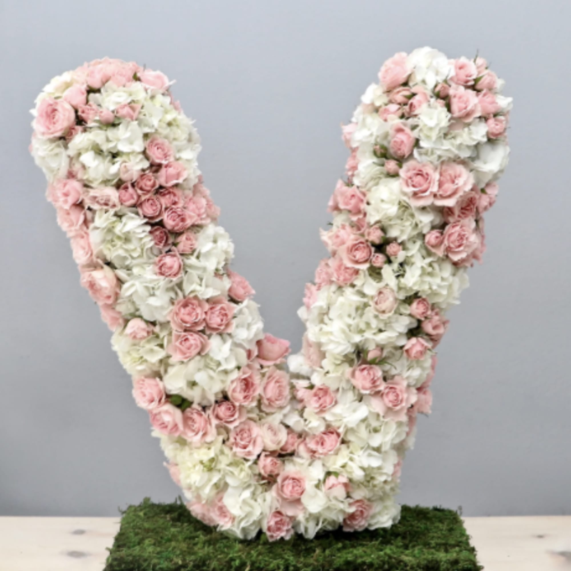Large pink and white floral letter V standing upright on a moss-covered base