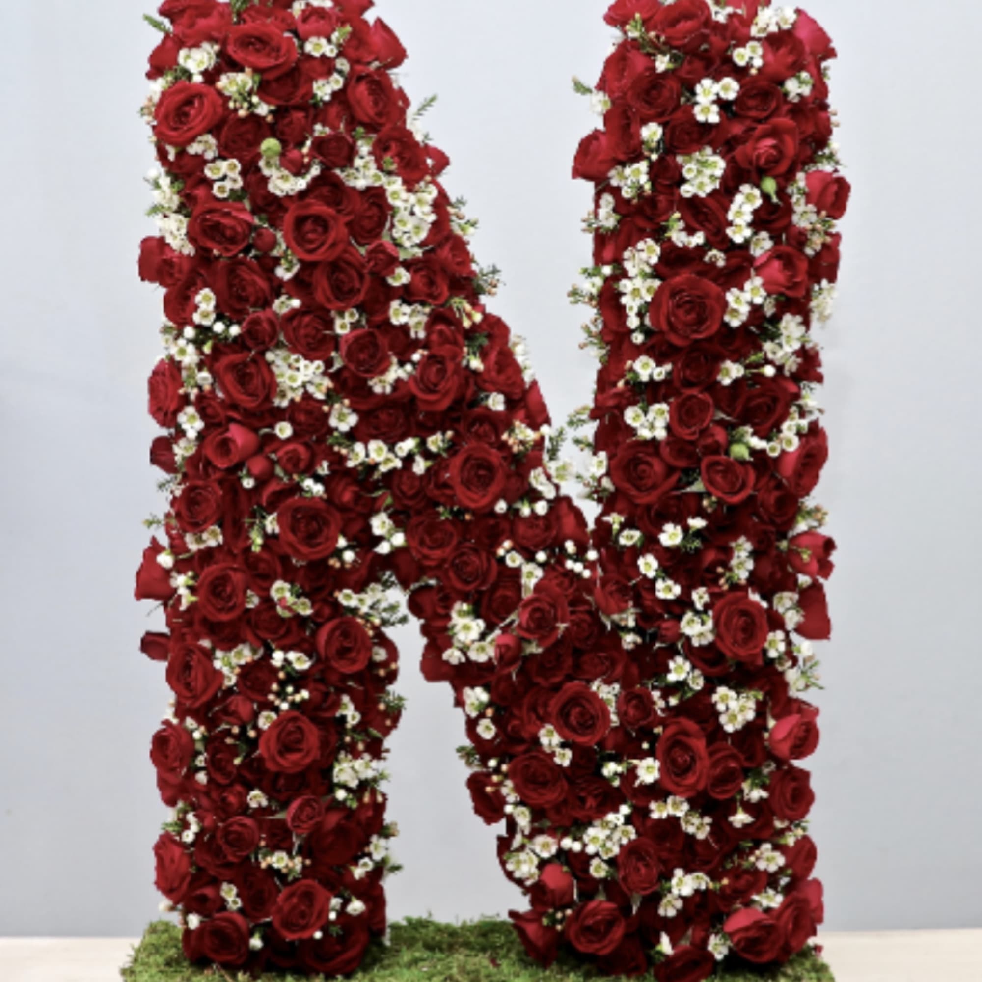 Large letter N made of red roses and small white flowers on a moss-covered base