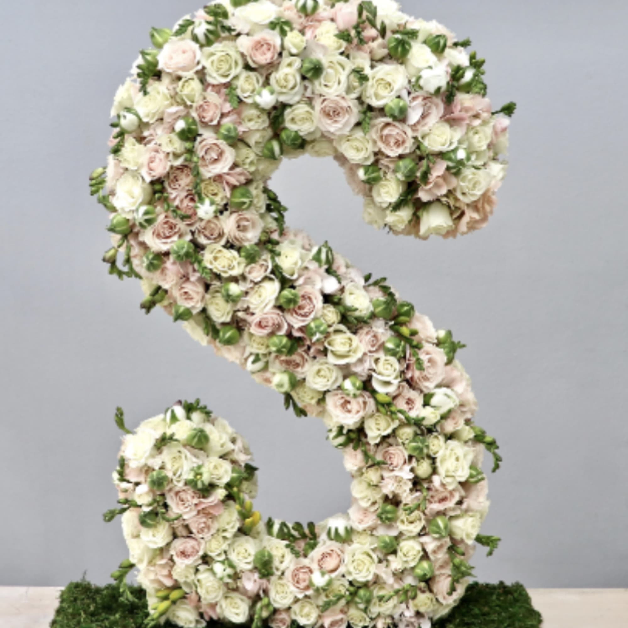 Tall floral letter S made of ivory and blush roses on a moss-covered base