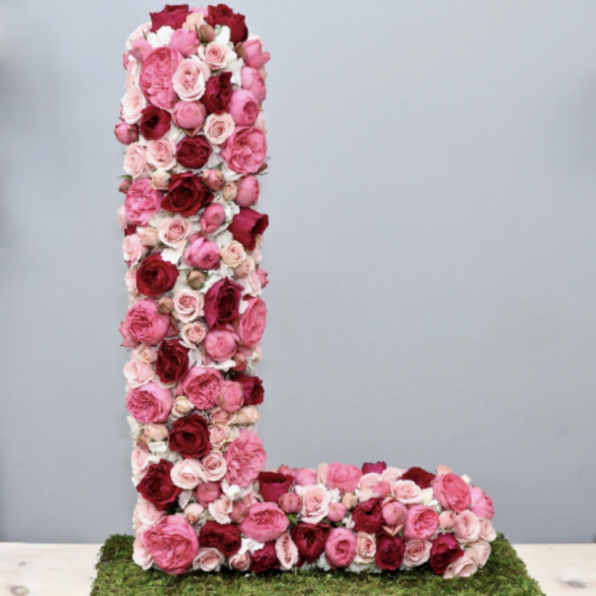 Floral letter L made of red and pink roses on a moss-covered base