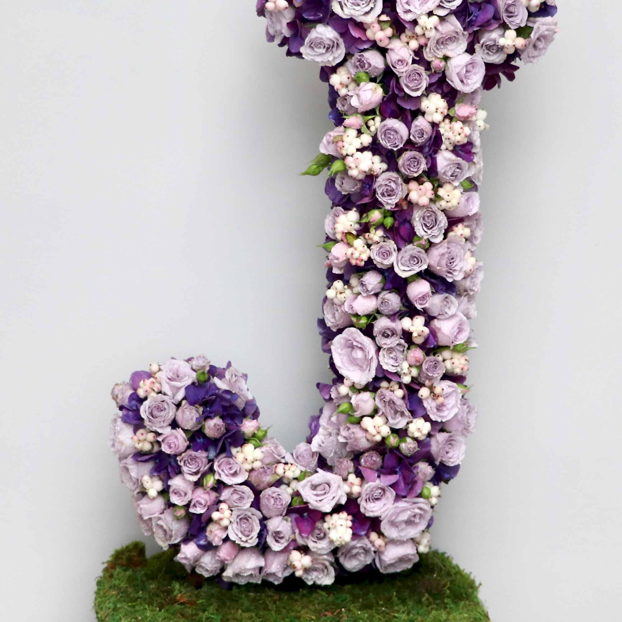 Tall floral letter J made of lavender and purple blooms on a moss-covered rectangular base