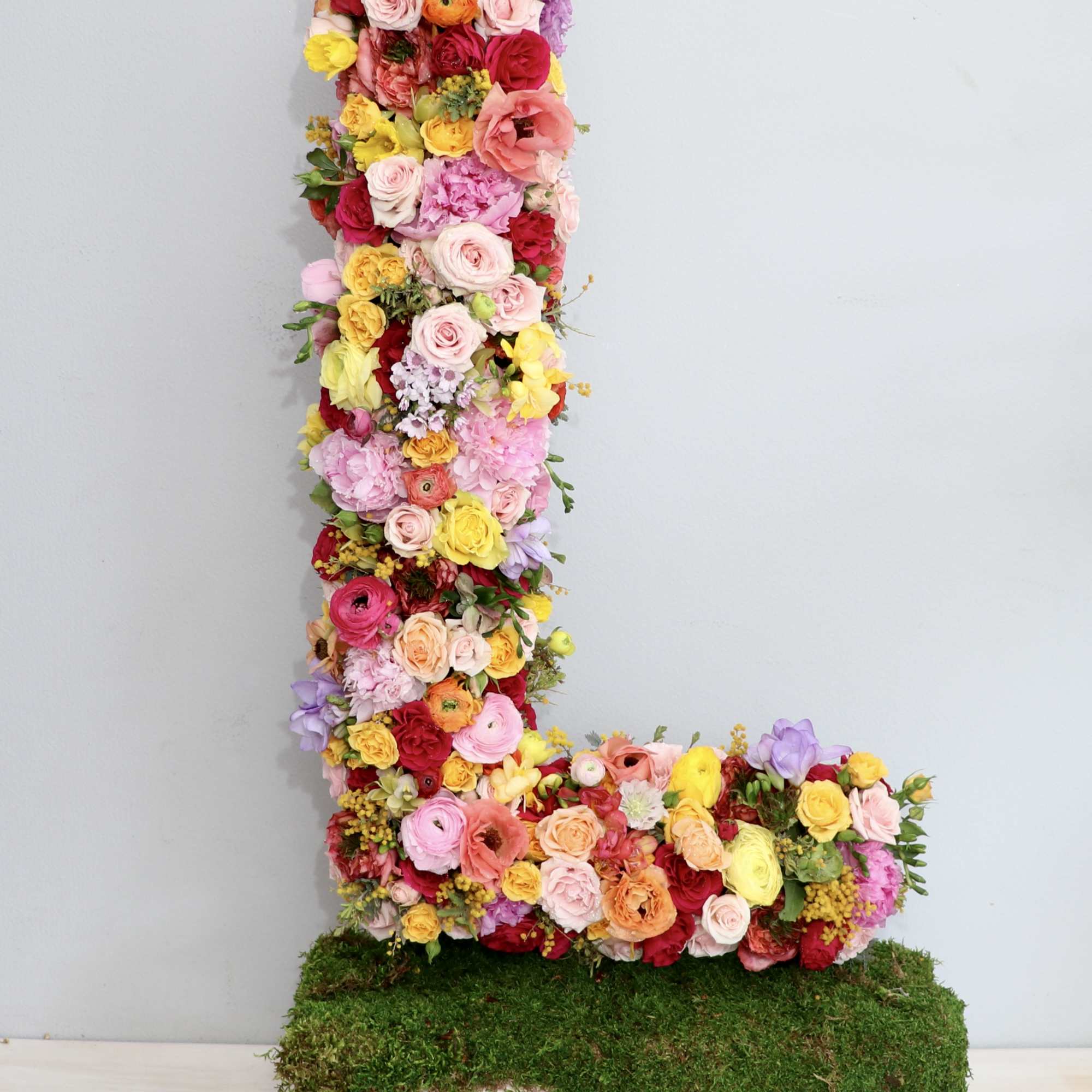 Tall floral letter L in bright mixed colors on a moss-covered wooden base