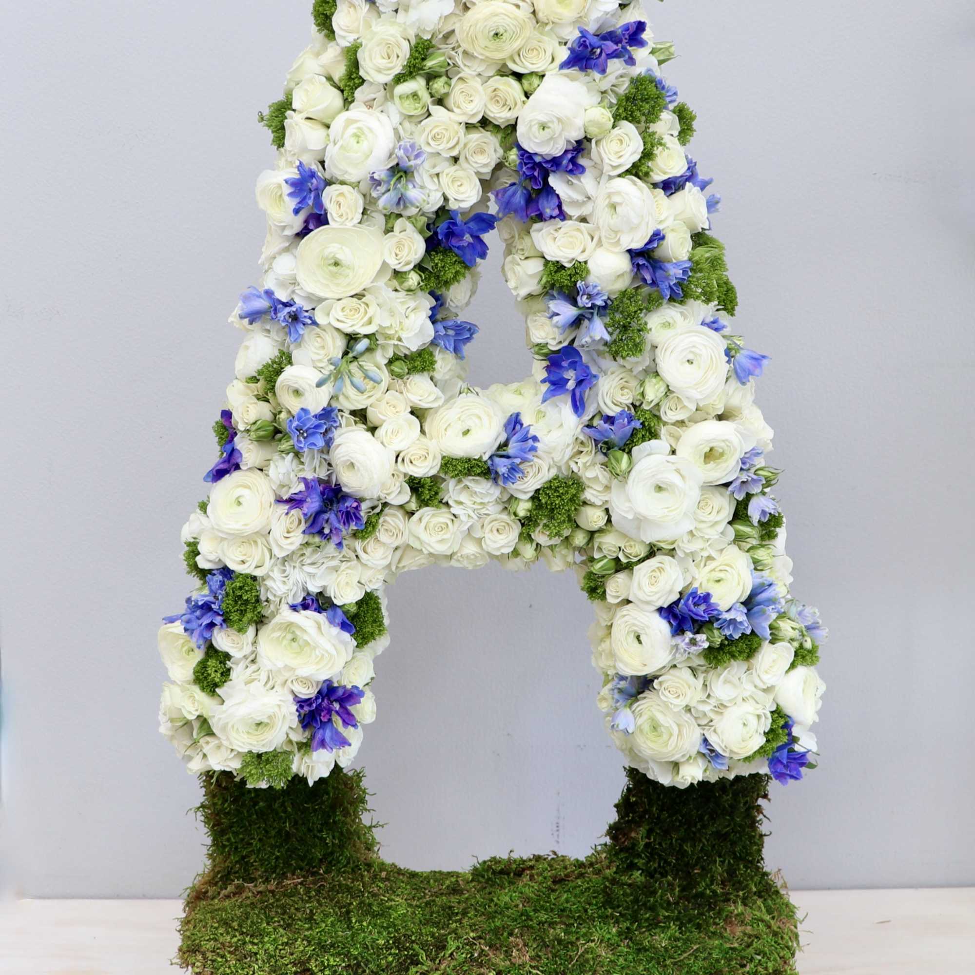 Tall floral letter A made of white blooms with blue accents on a moss-covered base