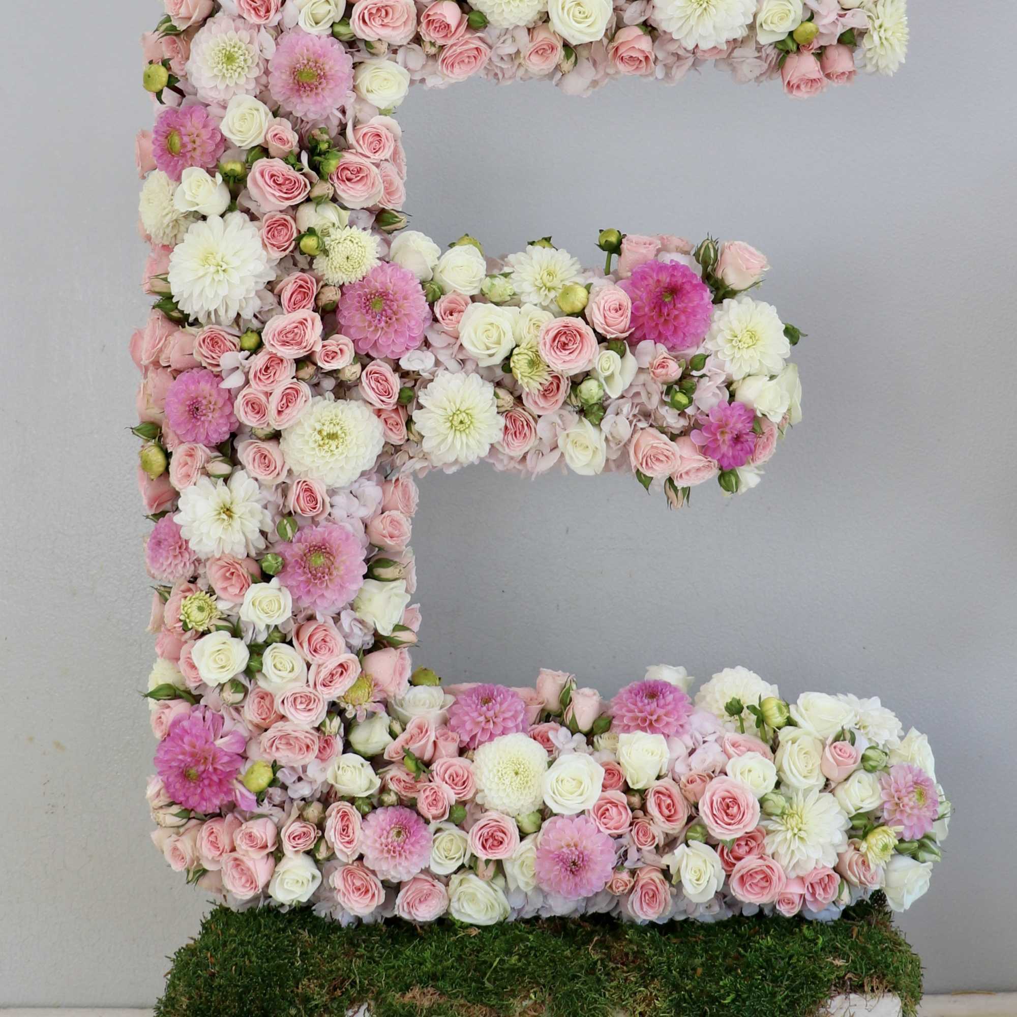 Large floral letter E made of pink and white flowers on a moss base