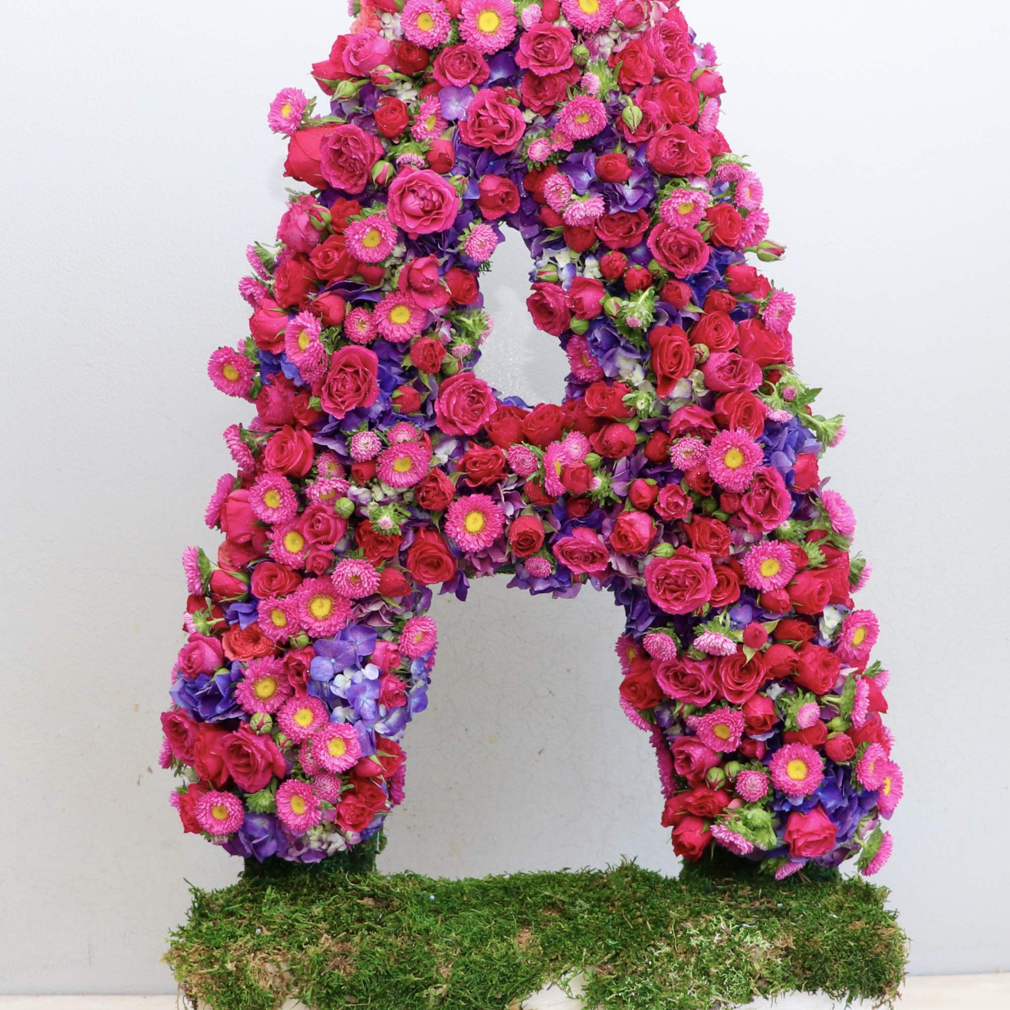 Large floral letter A covered in pink and purple flowers on a moss base