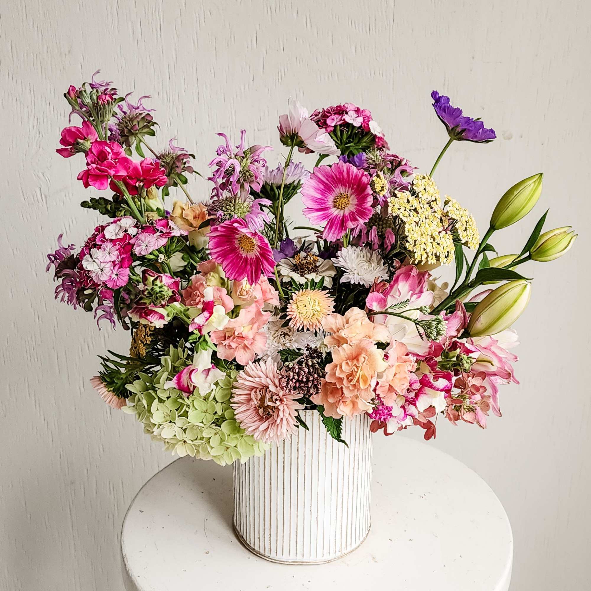 Mixed pink and purple flower arrangement in a white ribbed vase