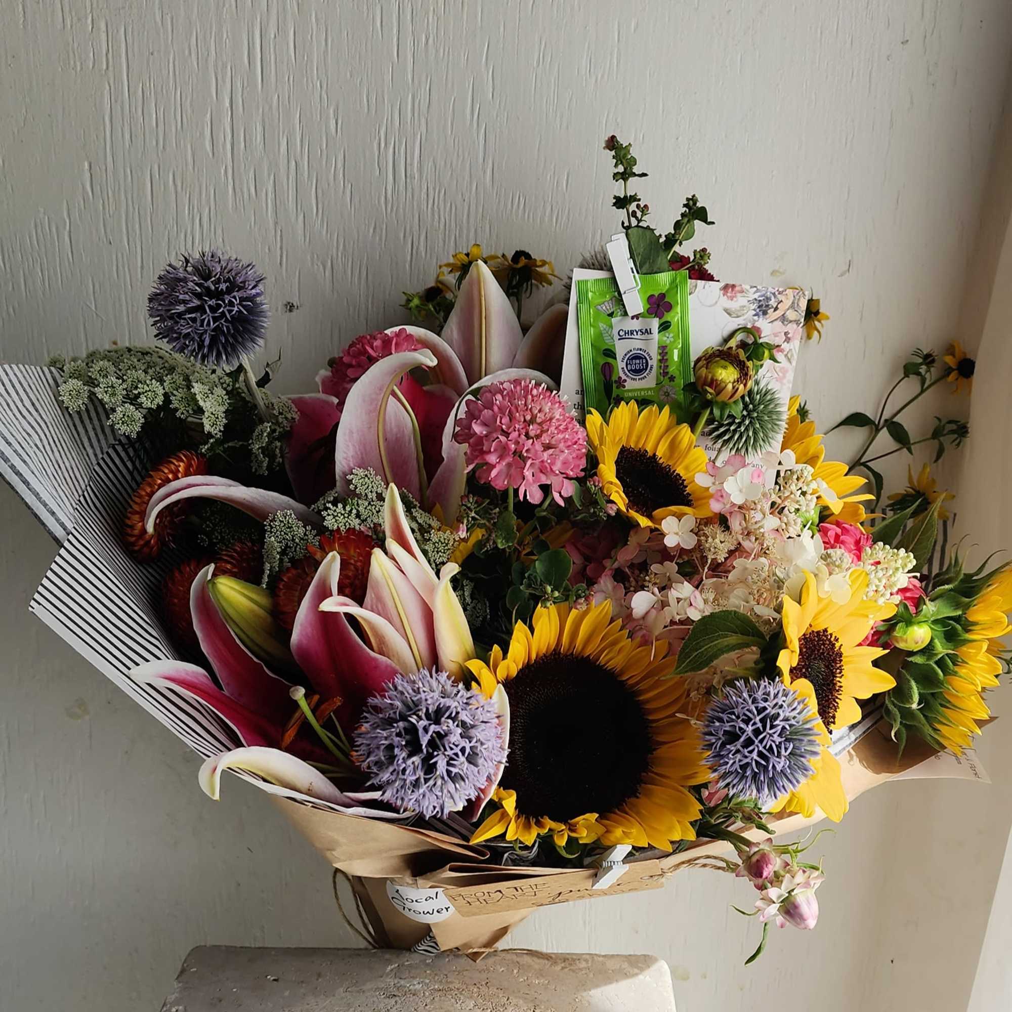Bouquet of sunflowers, lilies, and purple thistle-like blooms in paper wrap