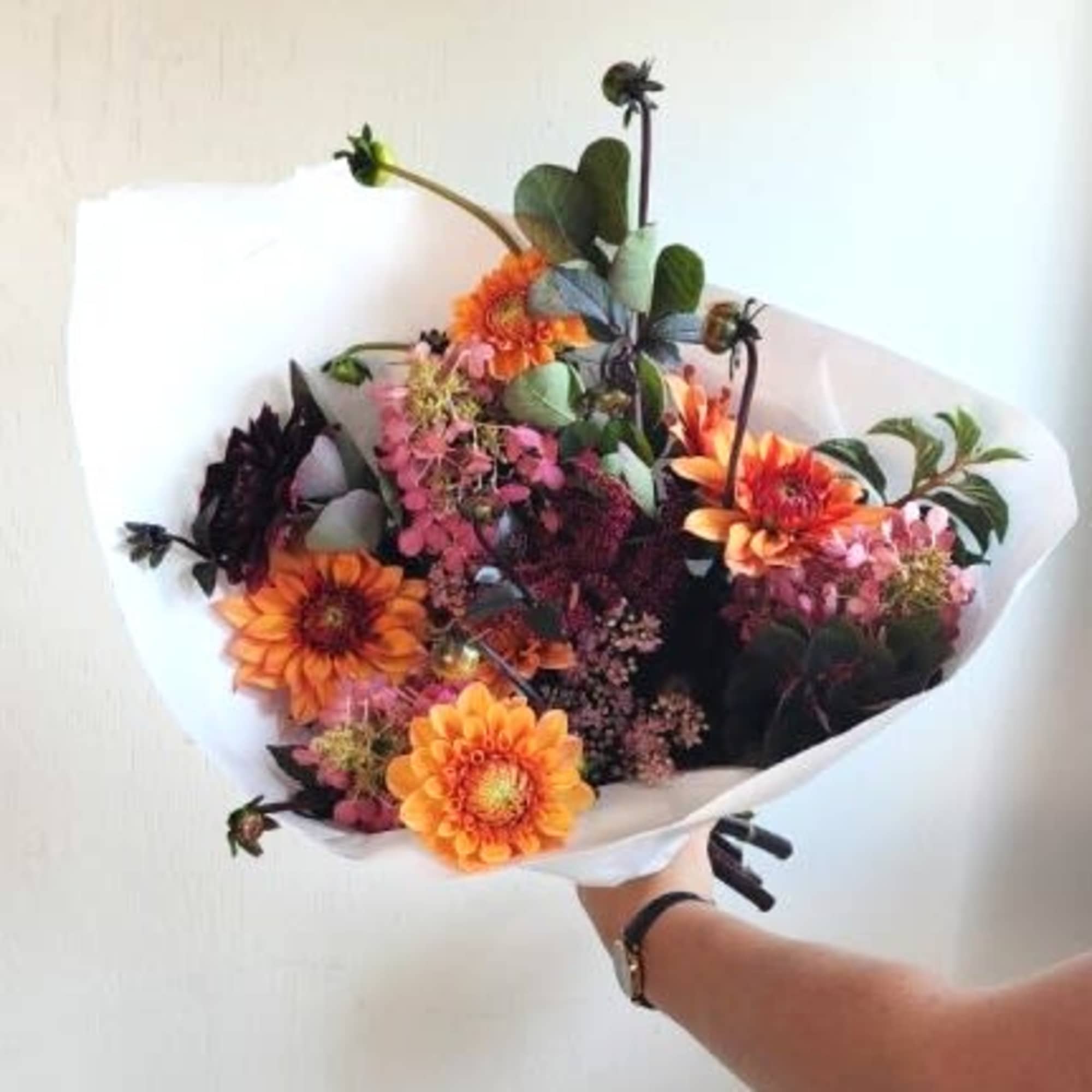 Handheld bouquet of orange and pink flowers wrapped in white paper