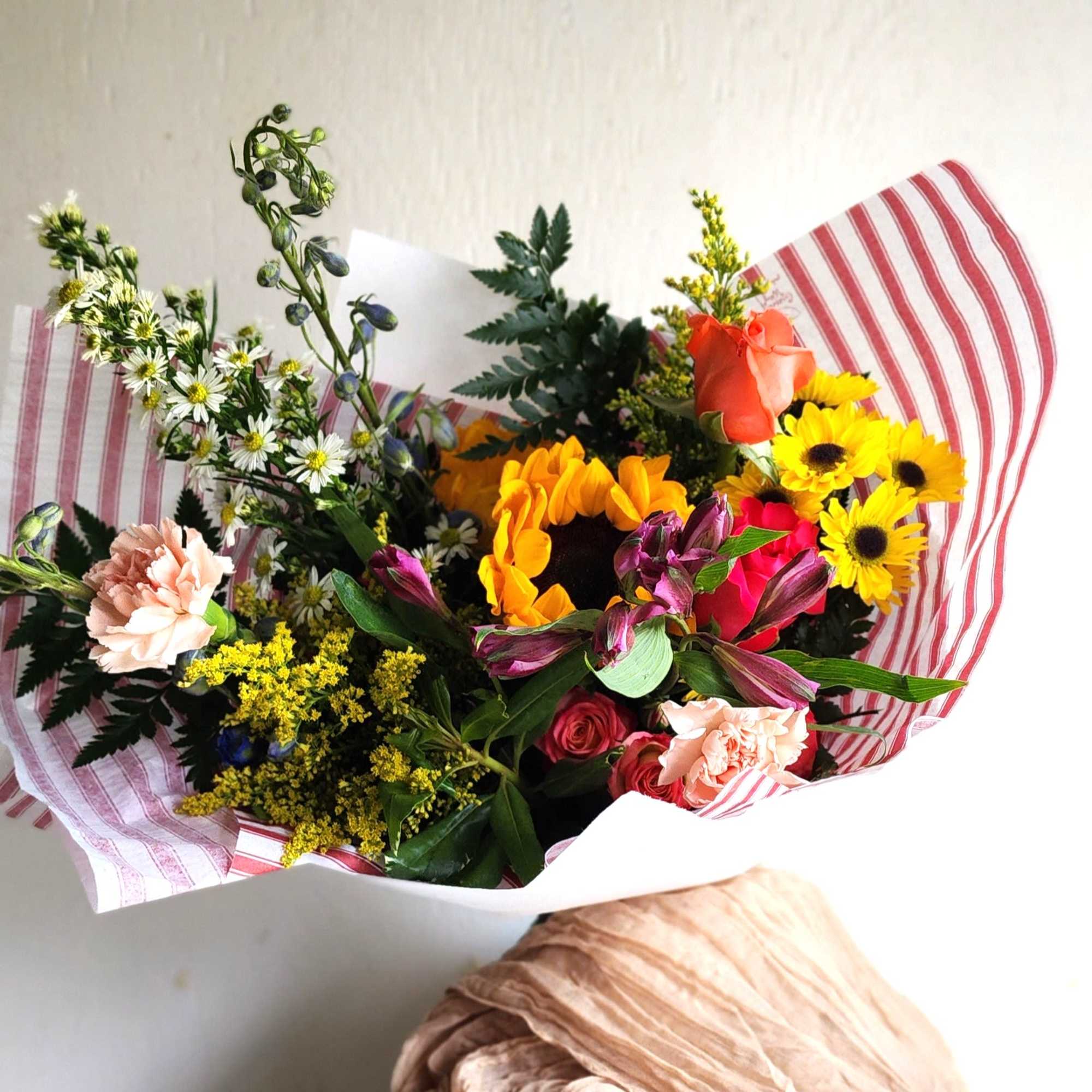 Mixed bouquet with sunflowers, roses, carnations, and daisies in striped wrap