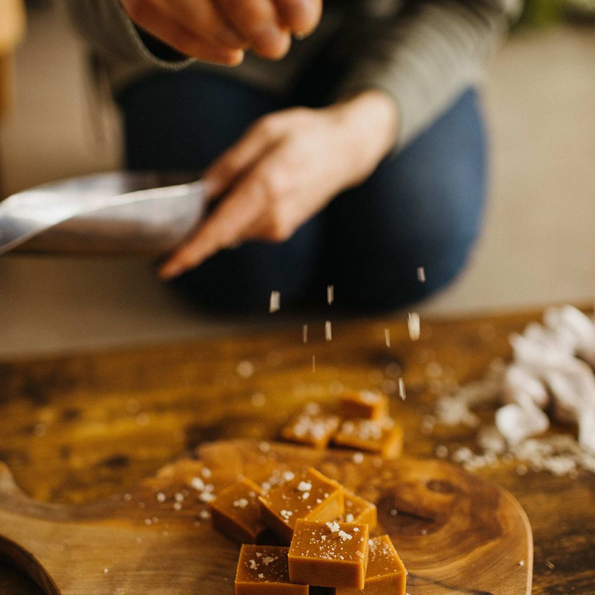 Hands sprinkling salt over caramel squares on a wooden board