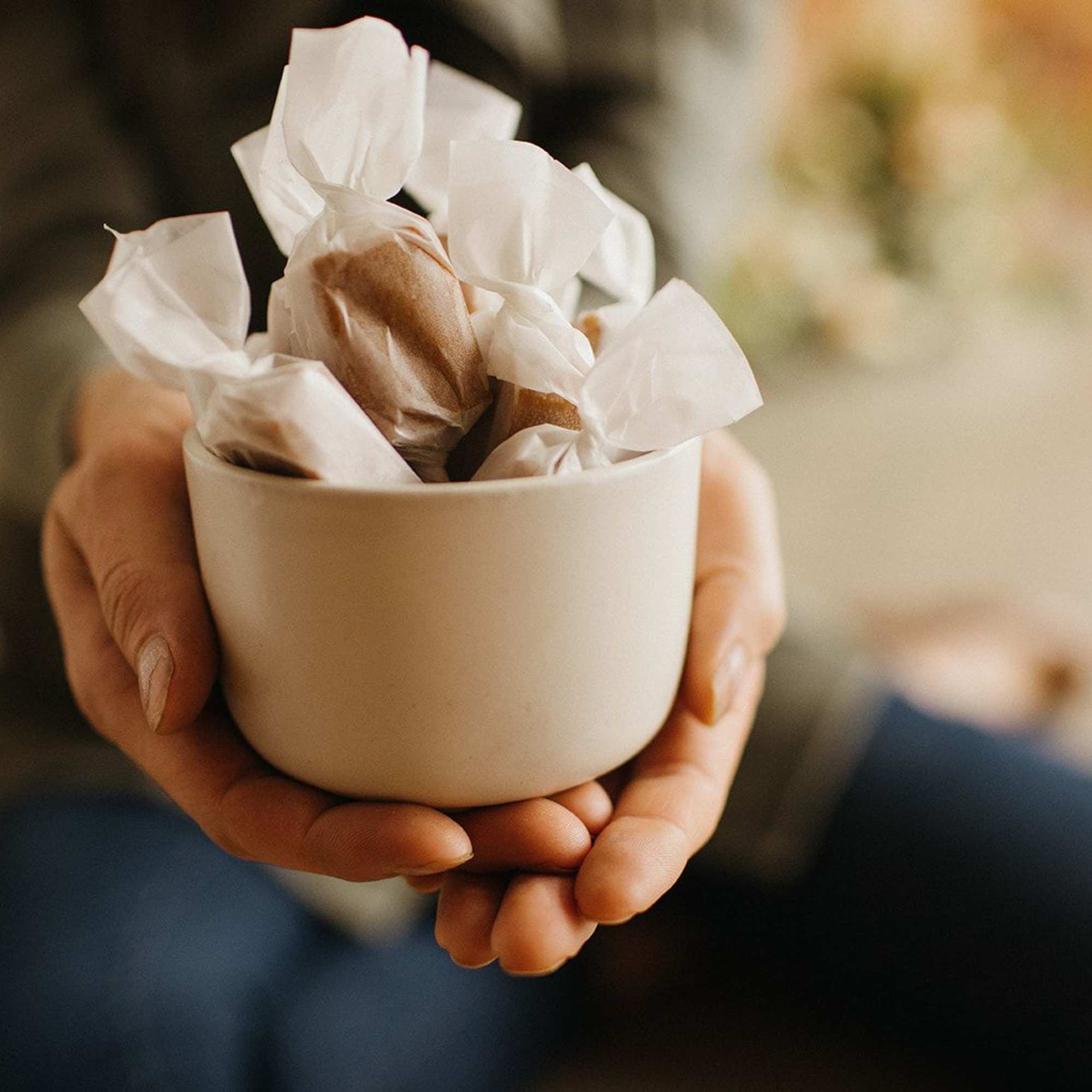 Hands holding a white bowl of wrapped chocolates