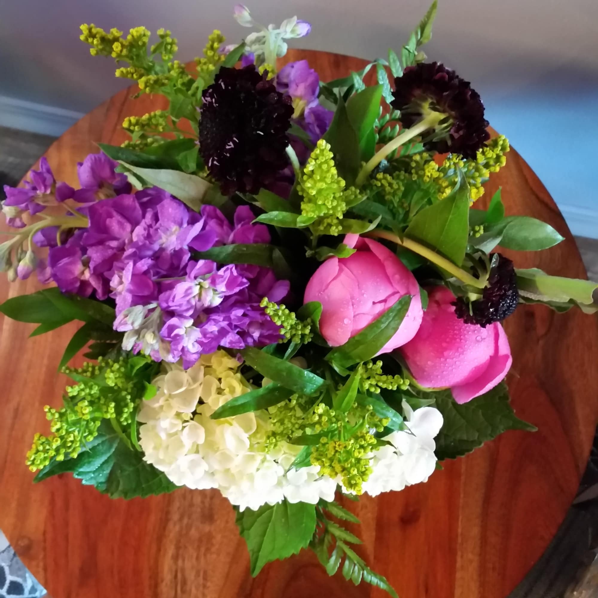 Mixed bouquet with pink, purple, white, and dark flowers on a round wooden table