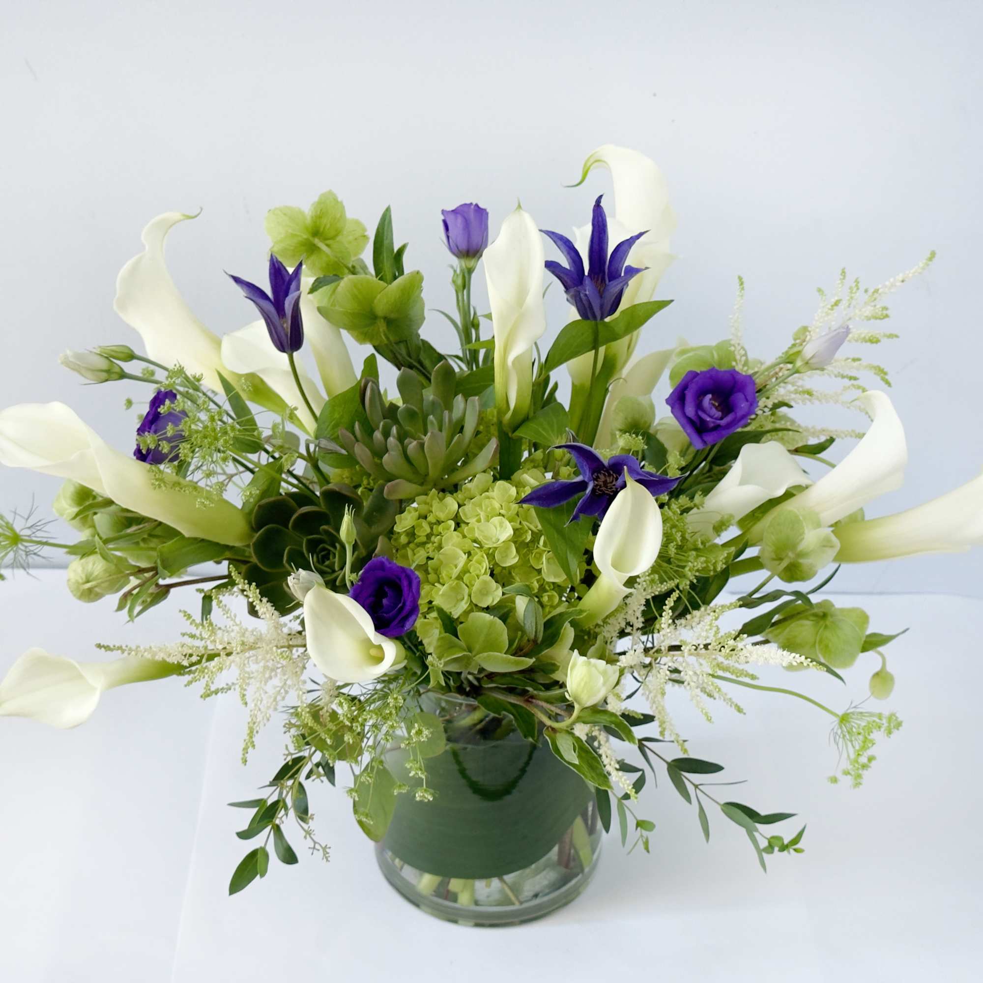 White calla lilies and purple flowers in a glass vase, photo 2 of 2