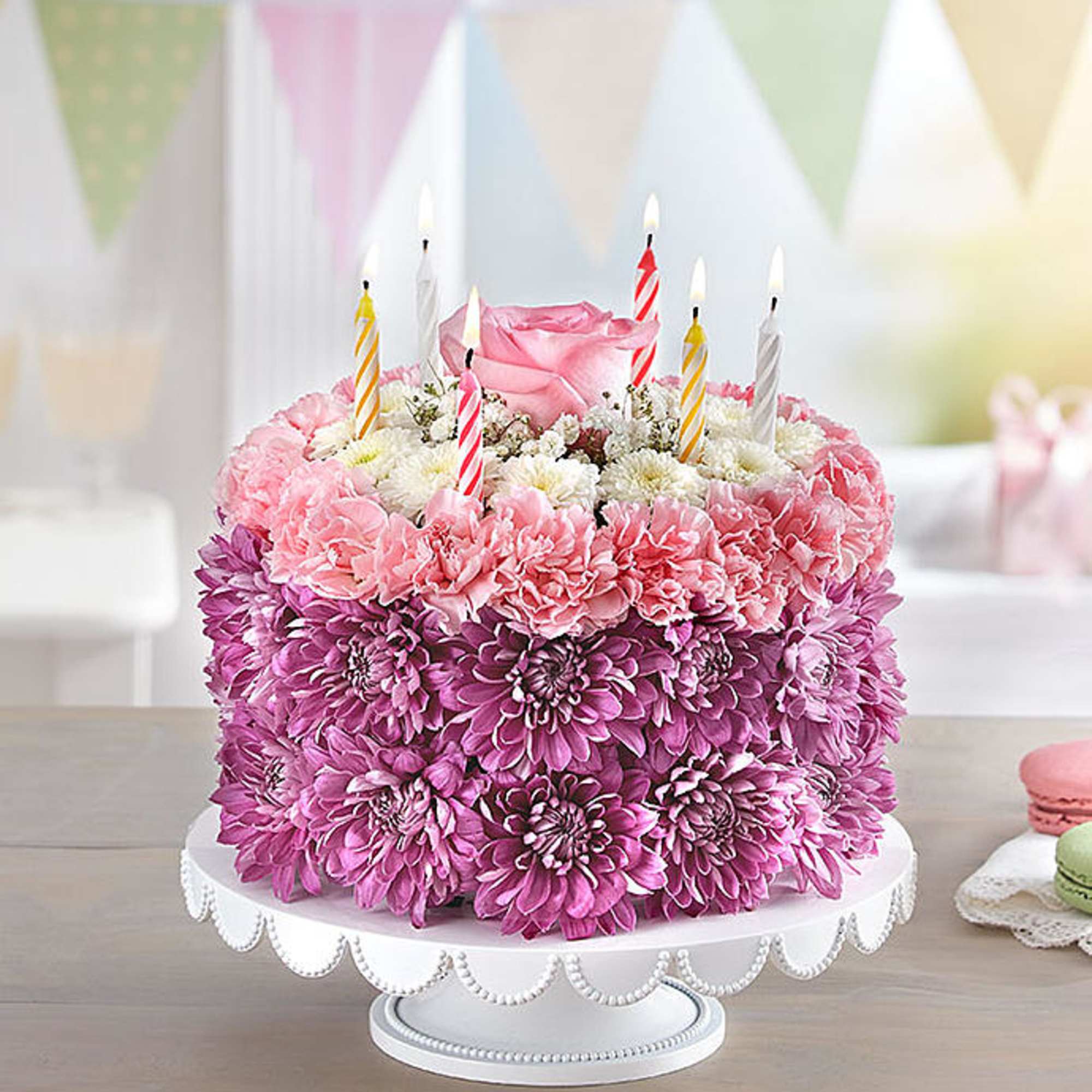 Pink floral cake with striped birthday candles on a white stand