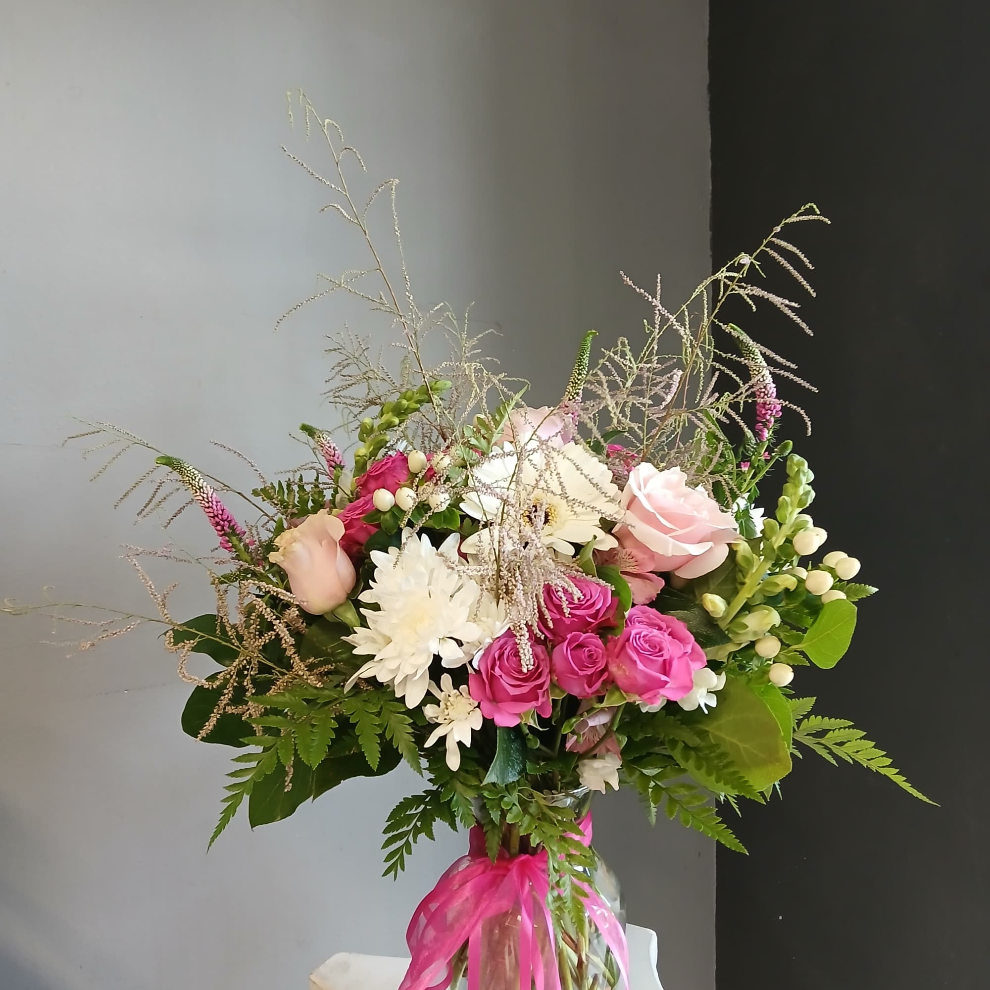 Bouquet of pink and white flowers in a glass vase with a pink ribbon