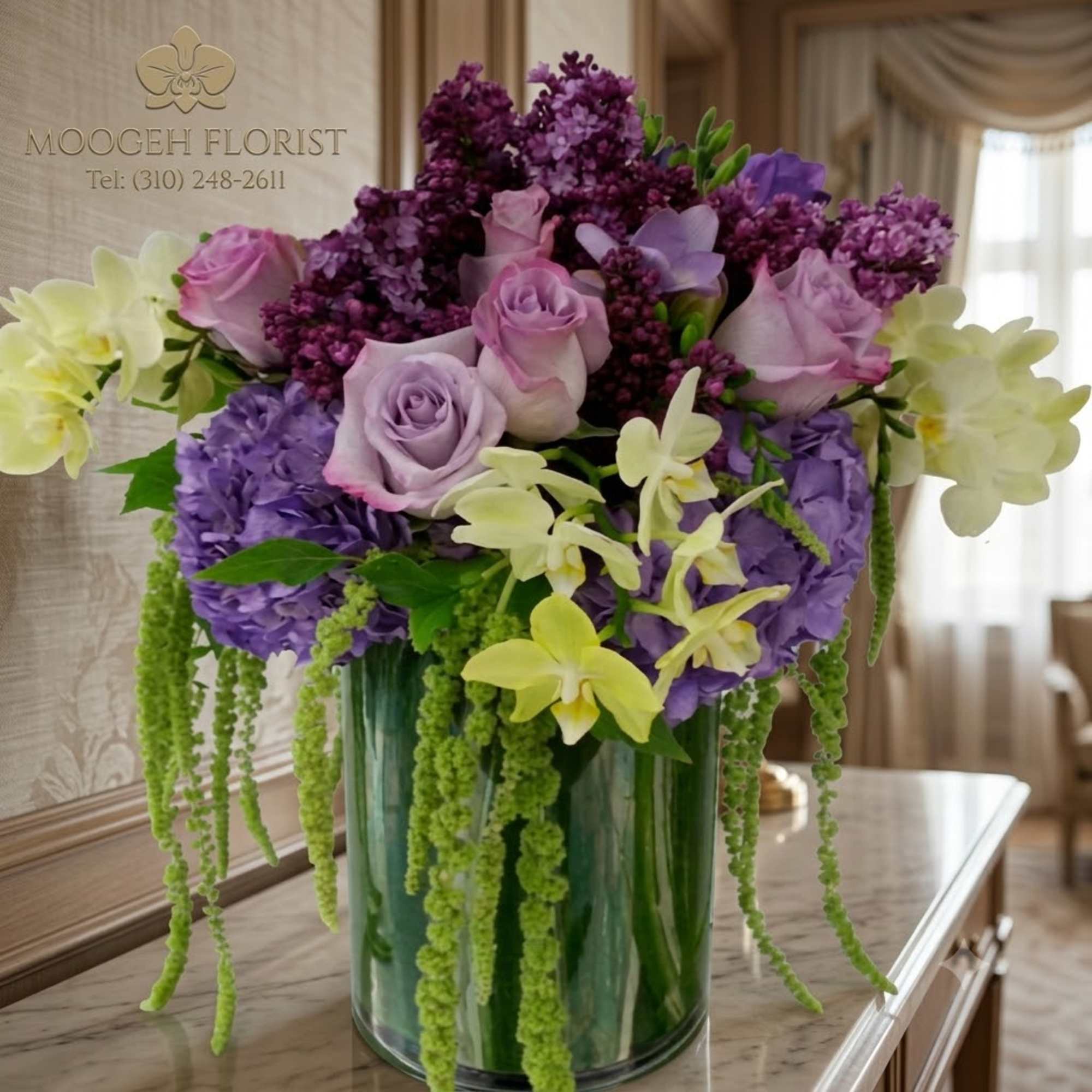 Purple and lavender floral arrangement in a glass vase with trailing green accents