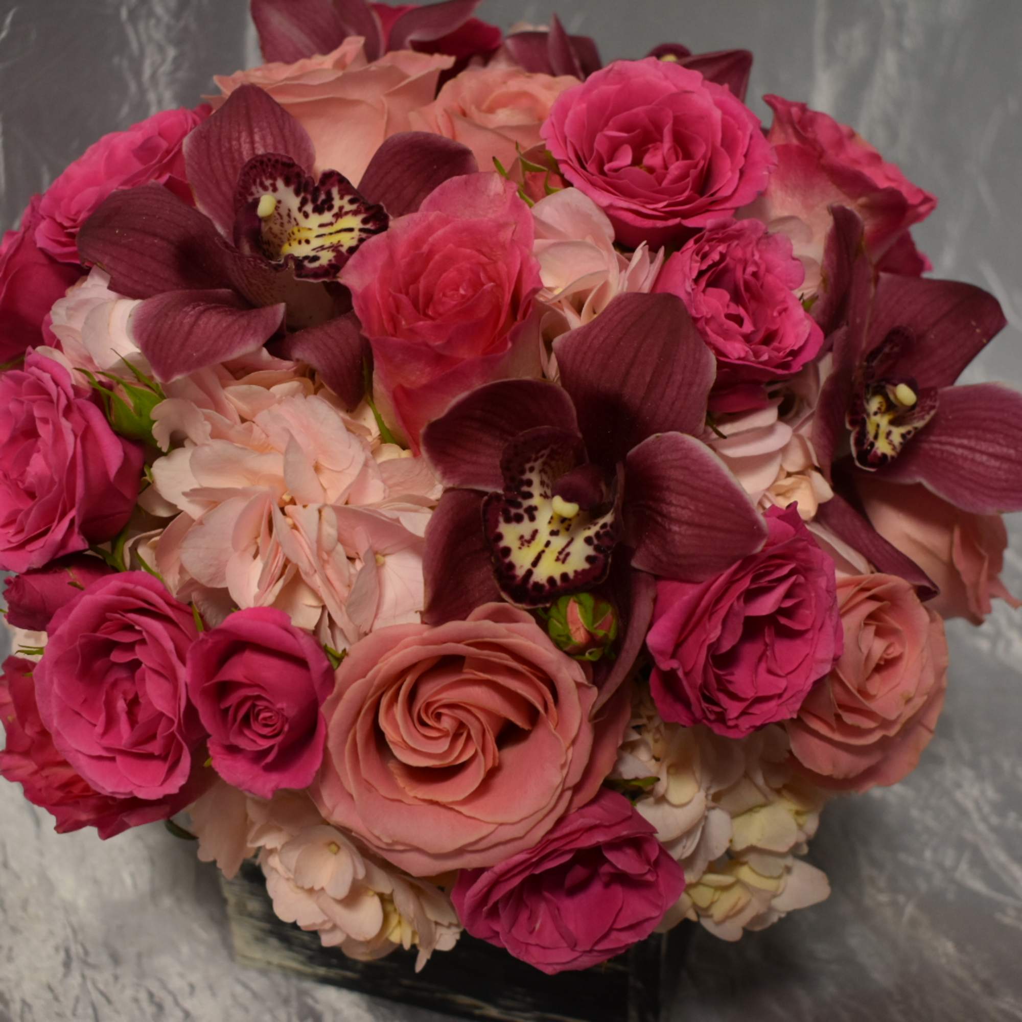 Round bouquet of pink roses and dark orchids in a low vase