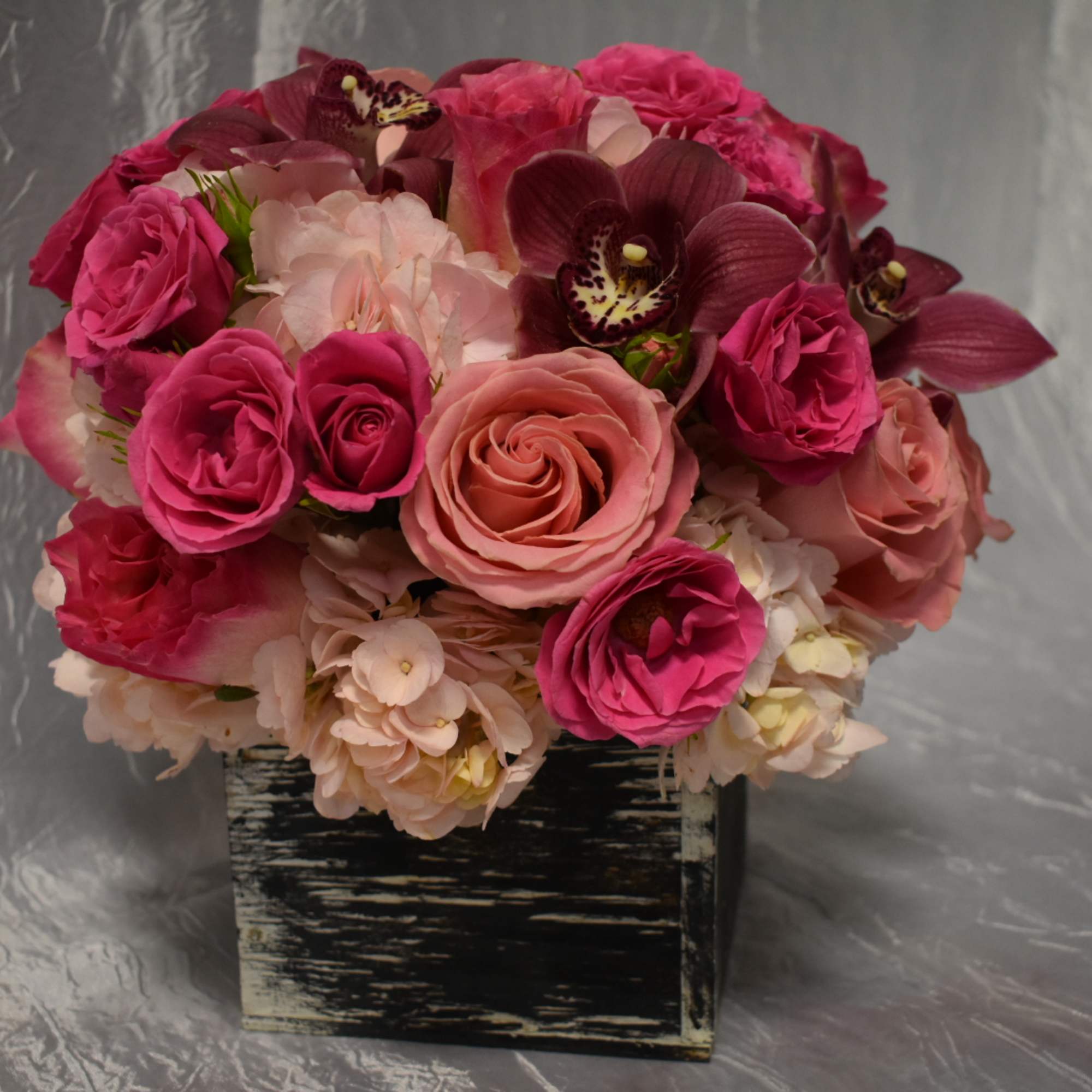 Pink and peach roses with orchids in a black square container