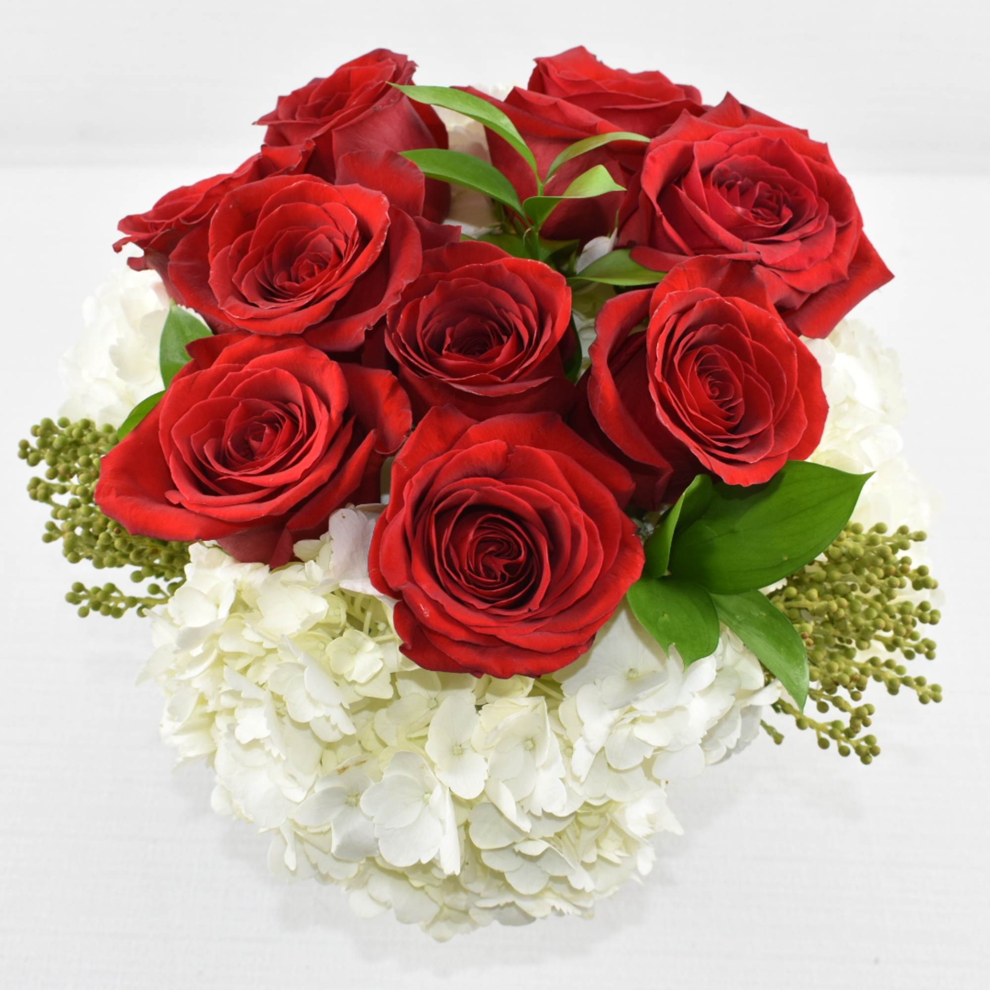 Round arrangement of red roses clustered over white hydrangeas in a clear glass vase.