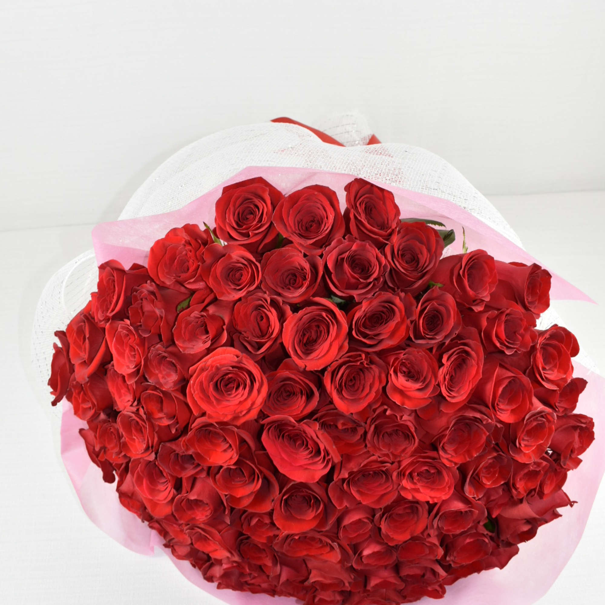 Large hand-tied bouquet of tightly clustered red roses wrapped in pink tissue and white mesh