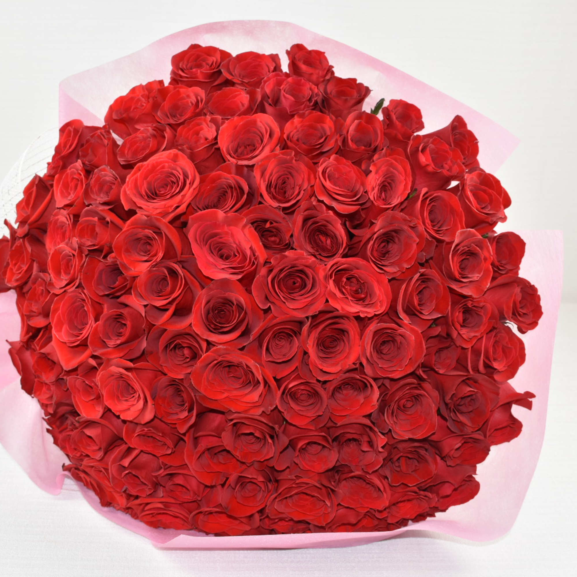 Large round bouquet of tightly packed red roses wrapped in pink paper