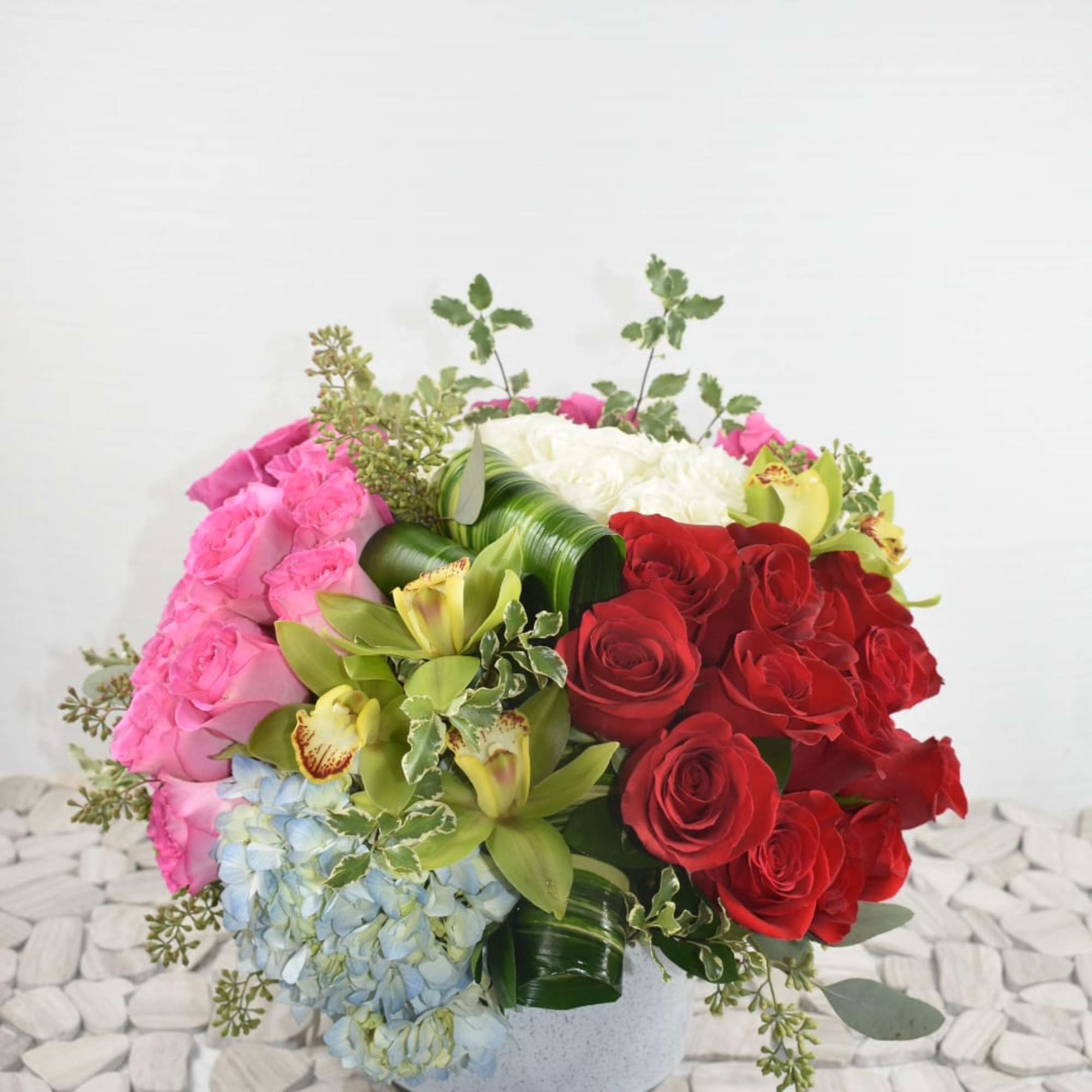 Round bouquet of pink and red roses with blue hydrangea in a white vase