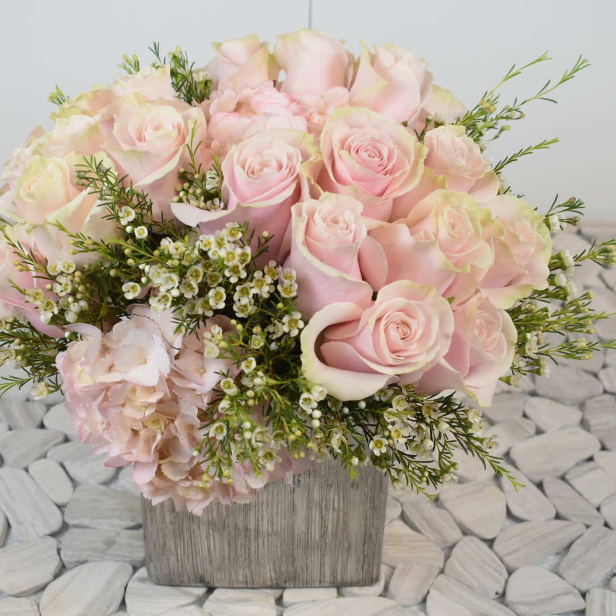 Pink roses and pale hydrangea in a square wooden vase