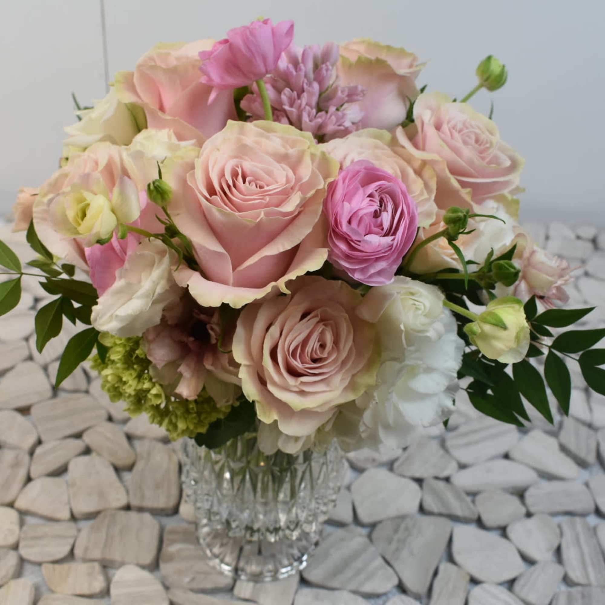 Round arrangement of blush pink roses and white blooms in a clear cut-glass vase