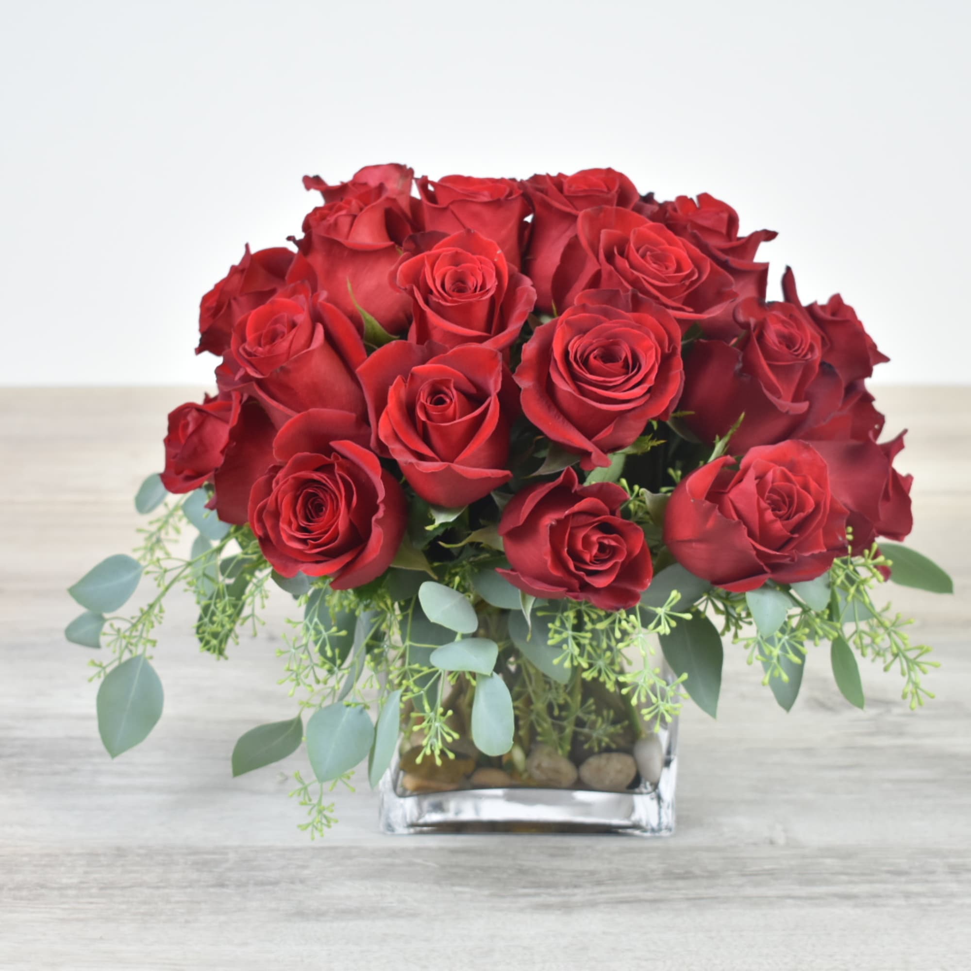 Low arrangement of red roses in a clear glass cube vase with trailing greenery