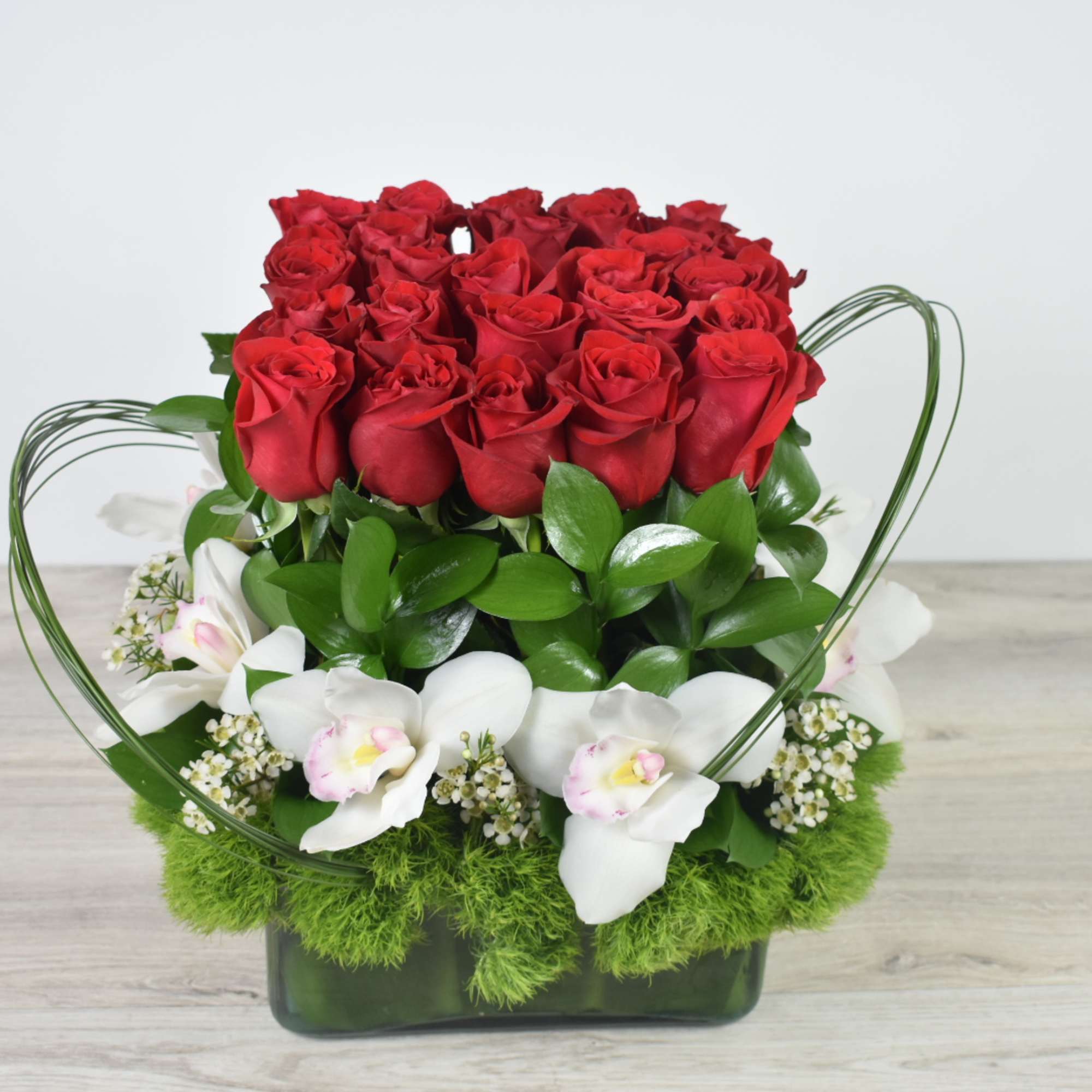 Compact arrangement of red roses and white orchids in a green glass vase with a collar of green moss